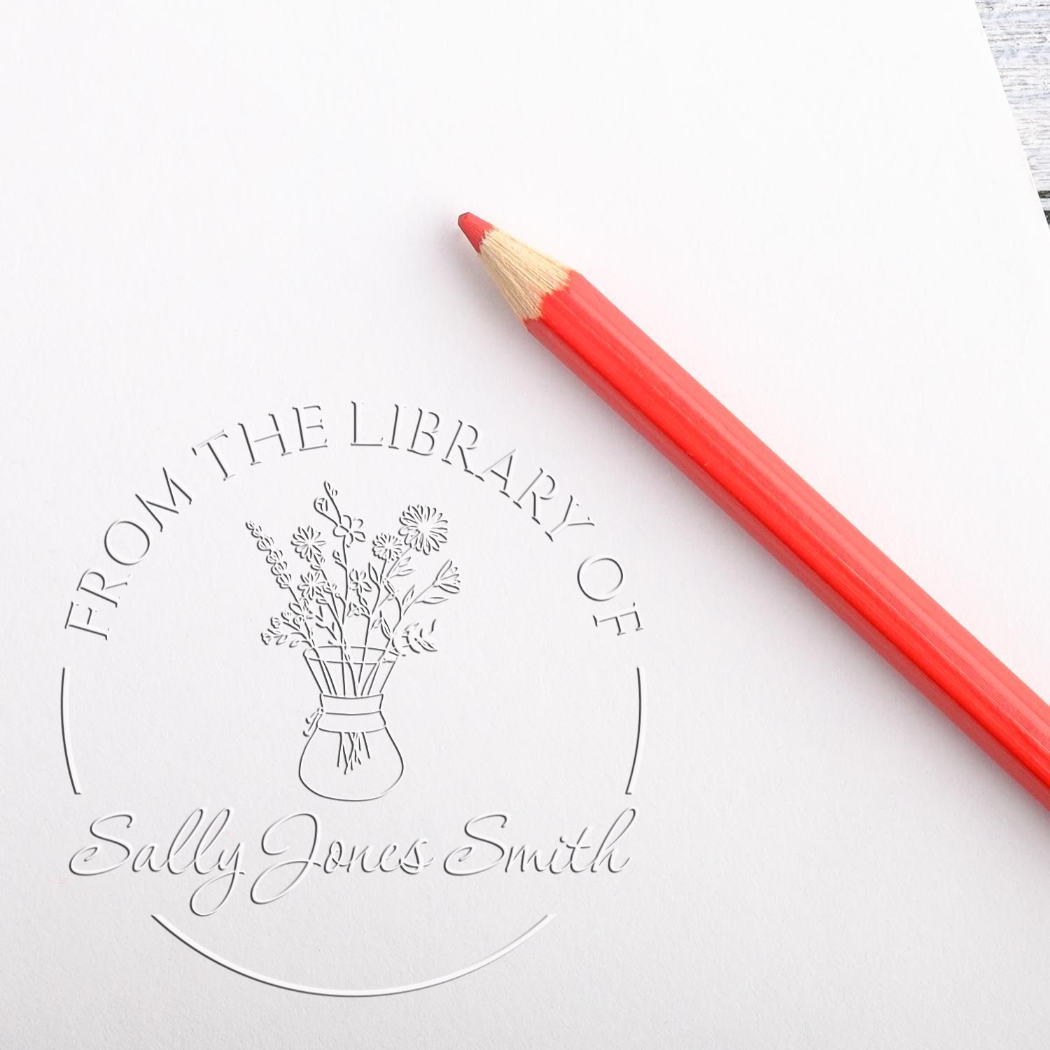Red pencil beside embossed library ownership stamp seal with flower vase and From the Library of Sally Jones Smith text.
