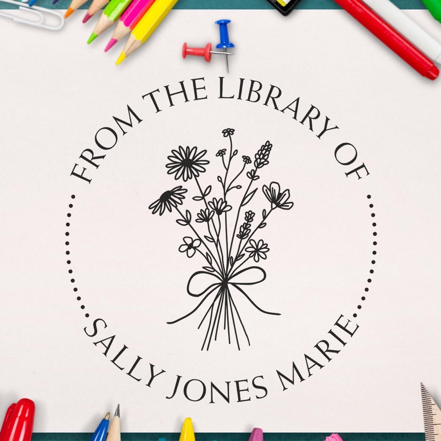 Custom black stamp seal with floral bouquet and Sally Jones Marie, surrounded by colorful pencils on white.