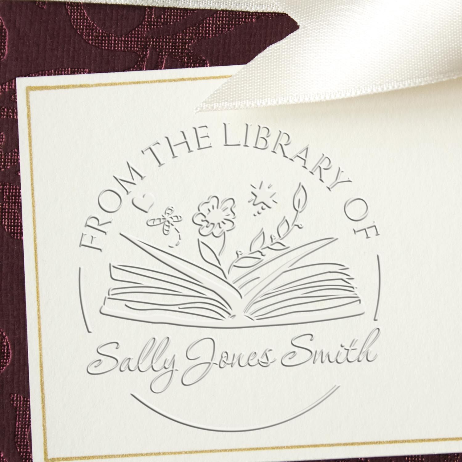 Embossed library stamp seal on cream card with gold border, reading From the Library of Sally Jones Smith, on burgundy background.