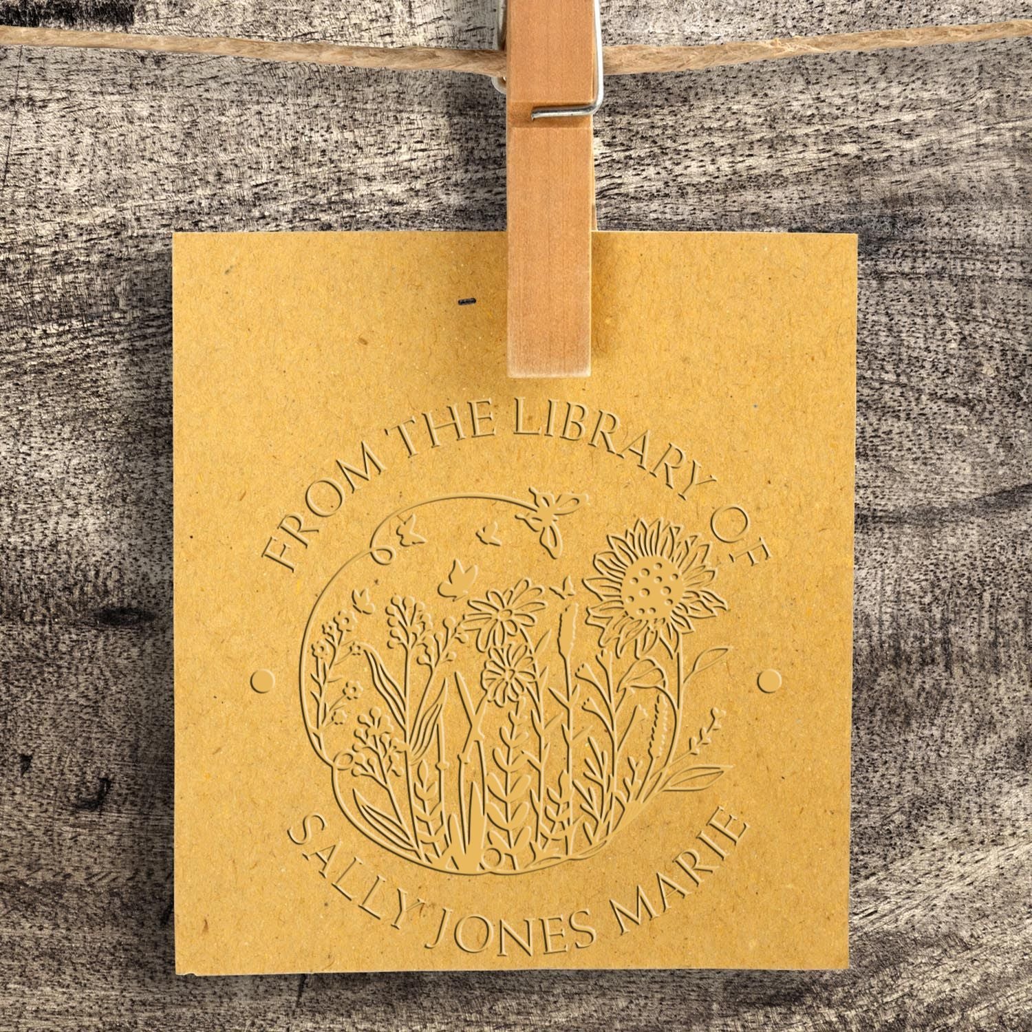 Gold embossed custom library stamp and seal with floral design, clipped to rustic wood background.