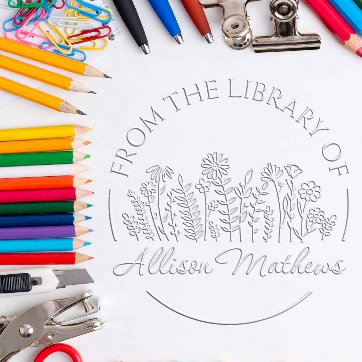 Custom embossed library seal stamp with colorful pencils, pens, paper clips, and metal office tools on white background.