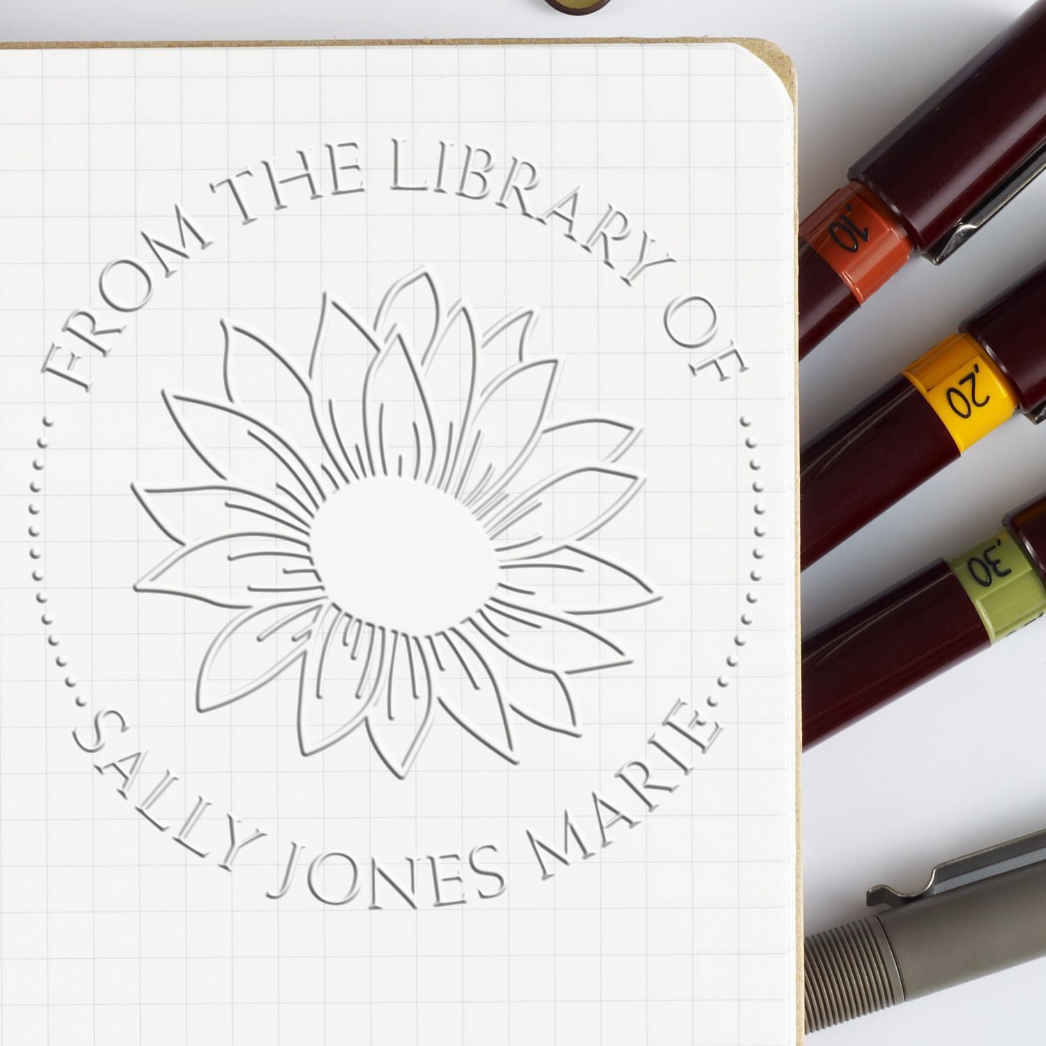 Embossed library seal on white grid paper with flower design, alongside burgundy, orange, yellow, green and gray stamp tools.