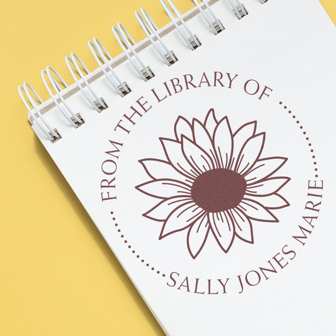 Brown sunflower book stamp and seal on a white spiral notebook against a yellow background