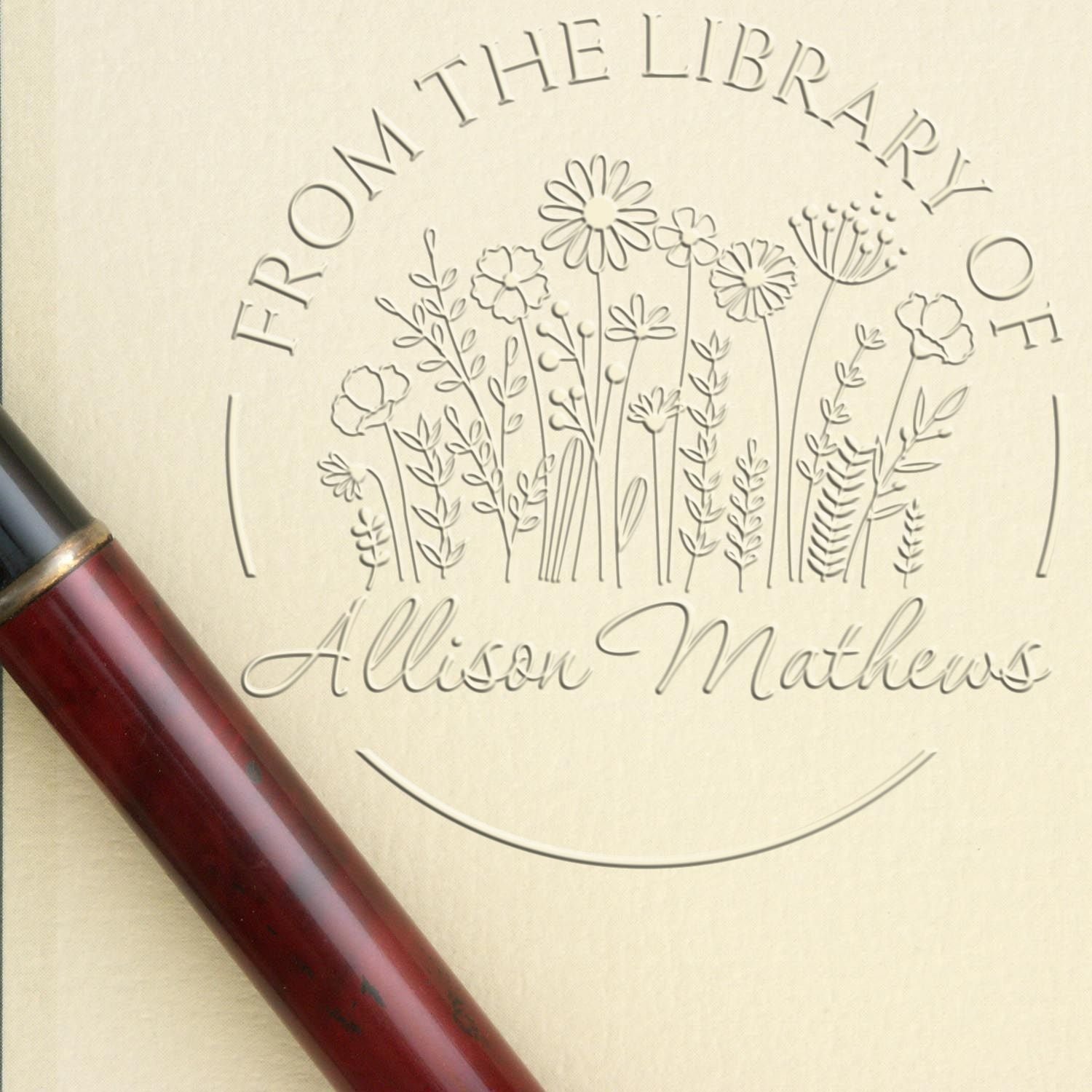 Cream custom stamp and seal with embossed wildflowers, library text, and Allison Matthews name, beside a burgundy handle.