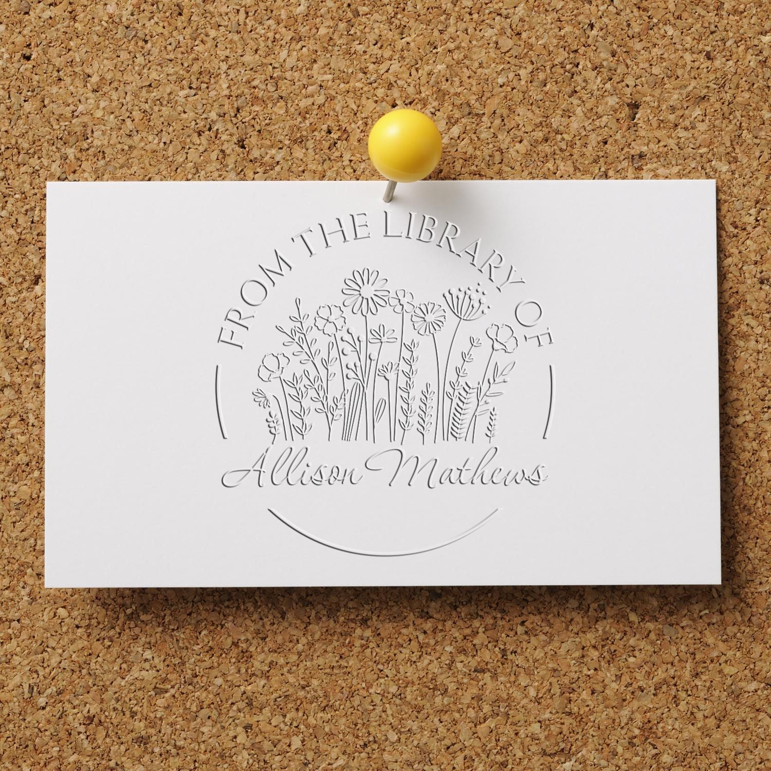 White embossed stamp and seal with floral bouquet and Allison Mathews, pinned with a yellow tack on a corkboard.