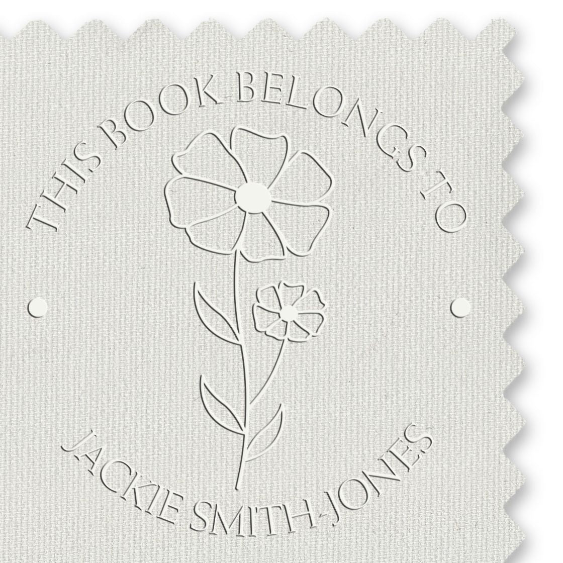 White embossed book stamp seal with floral logo and curved text "This Book Belongs to Jackie Smith-Jones"