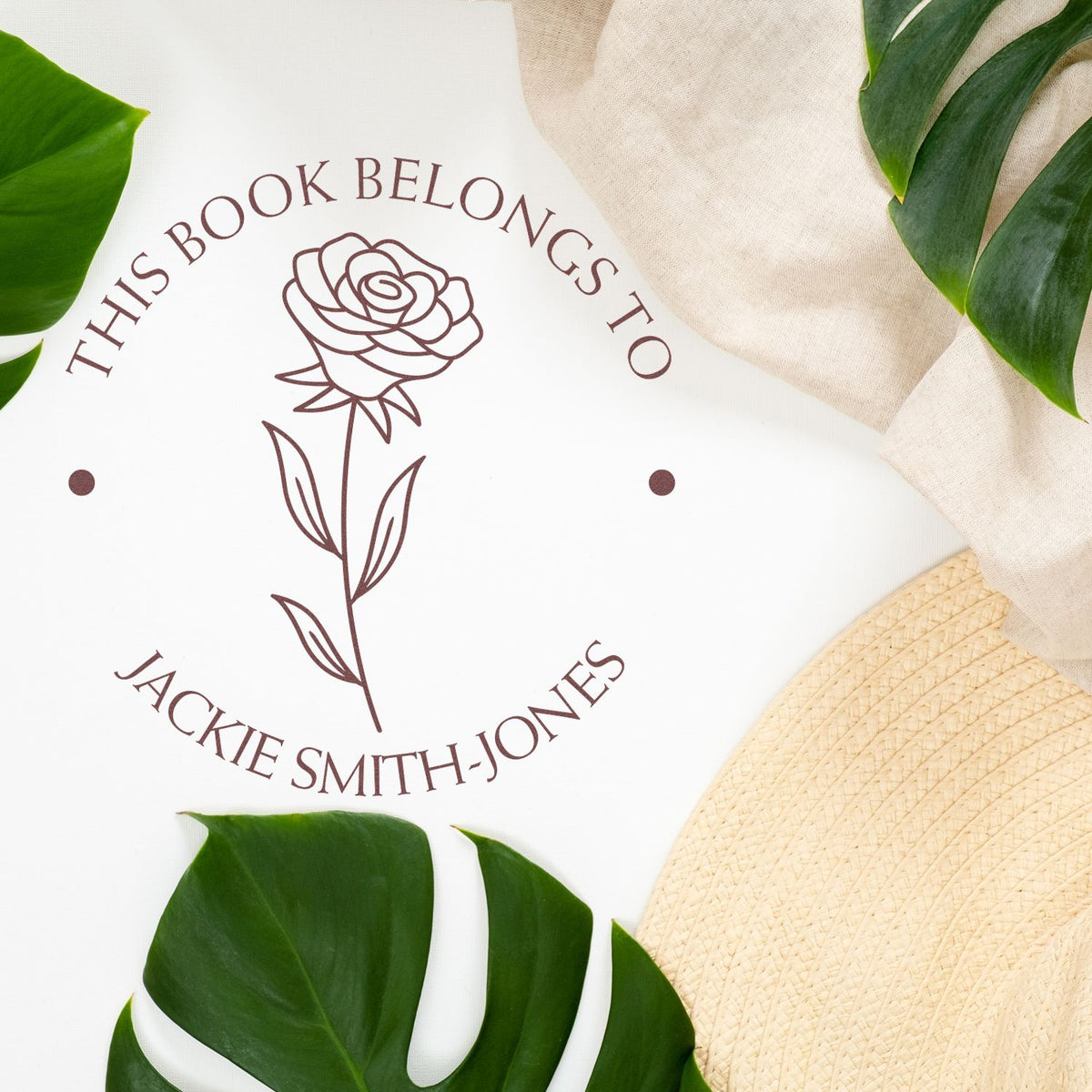 Brown rose custom book ownership stamp seal on white, framed by green leaves and beige fabric, with Jackie Smith-Jones text.