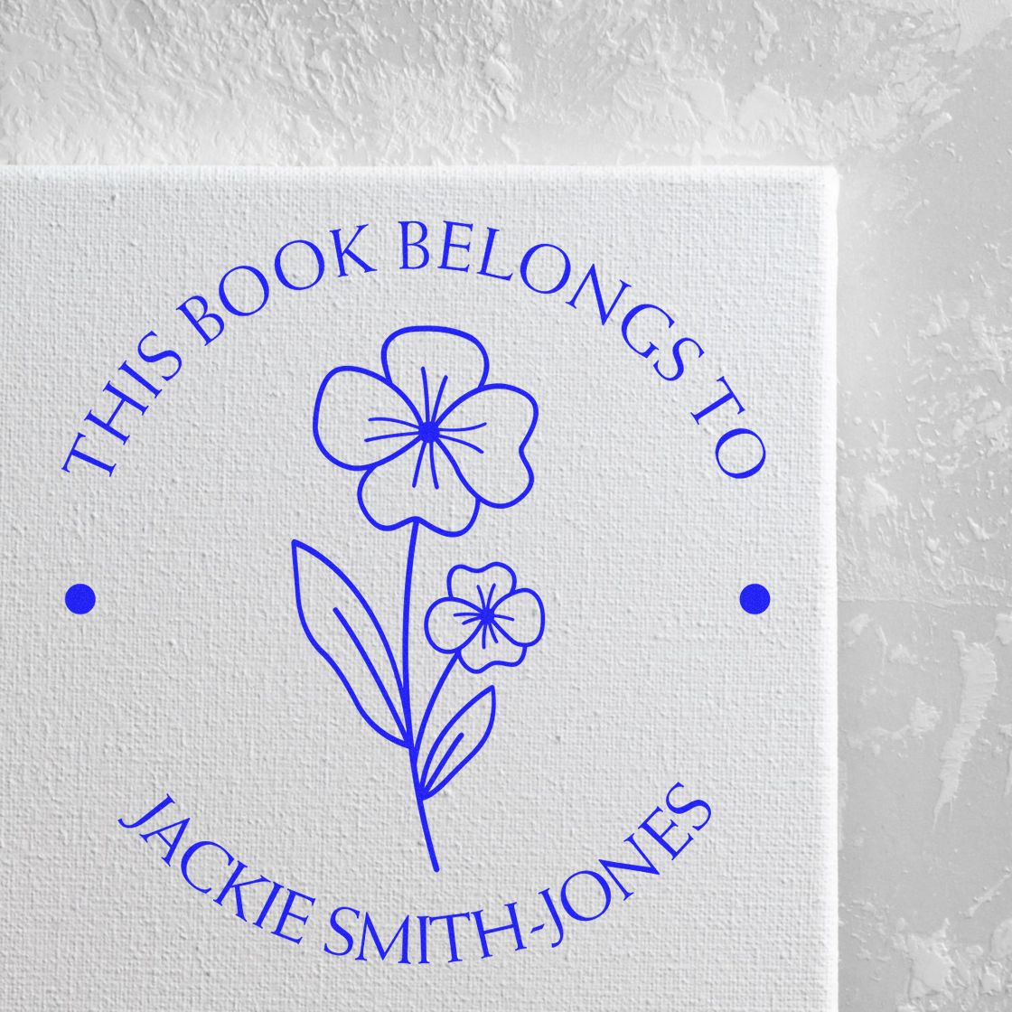 Blue custom book stamp/seal with floral design and This Book Belongs to Jackie Smith-Jones on white canvas.