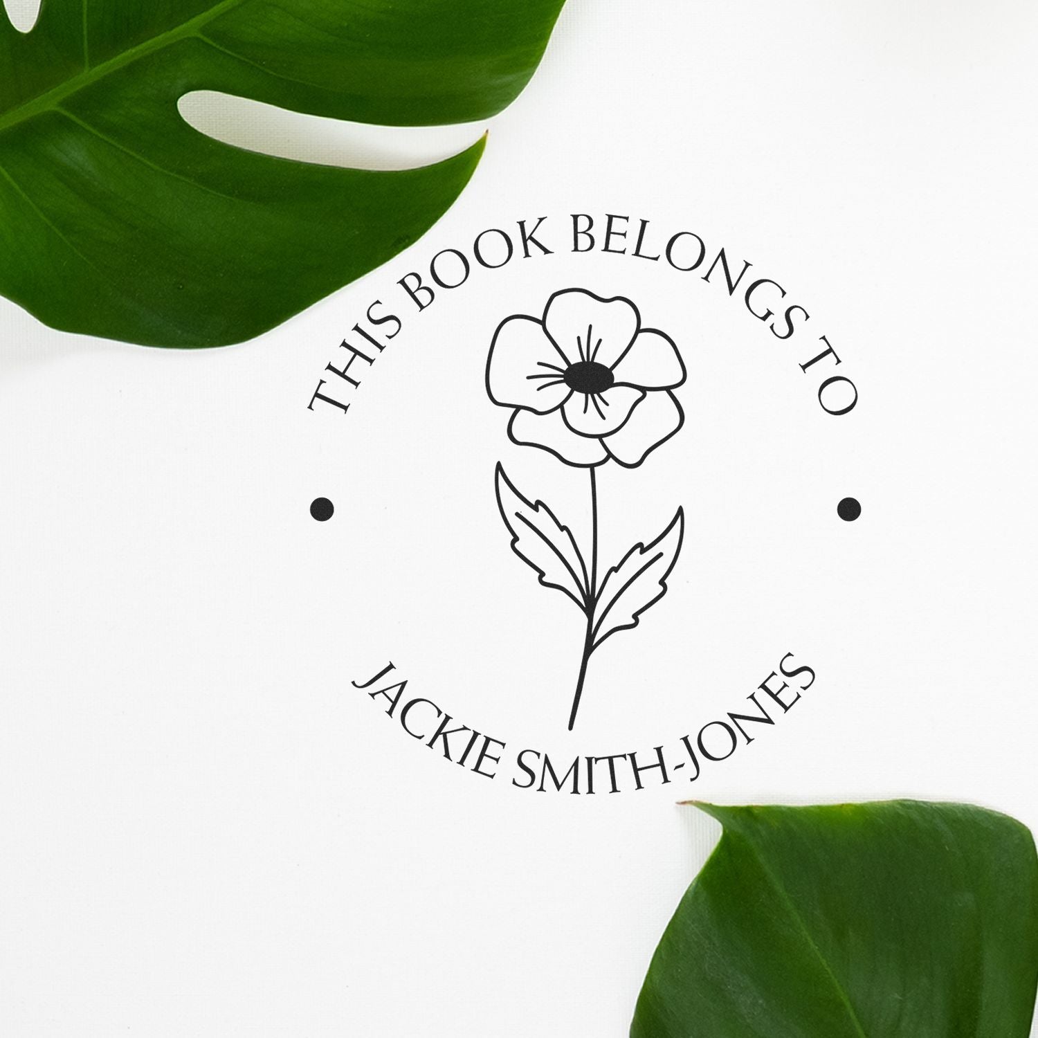 Black personalized bookplate stamp and seal with floral design on white, framed by green leaves.