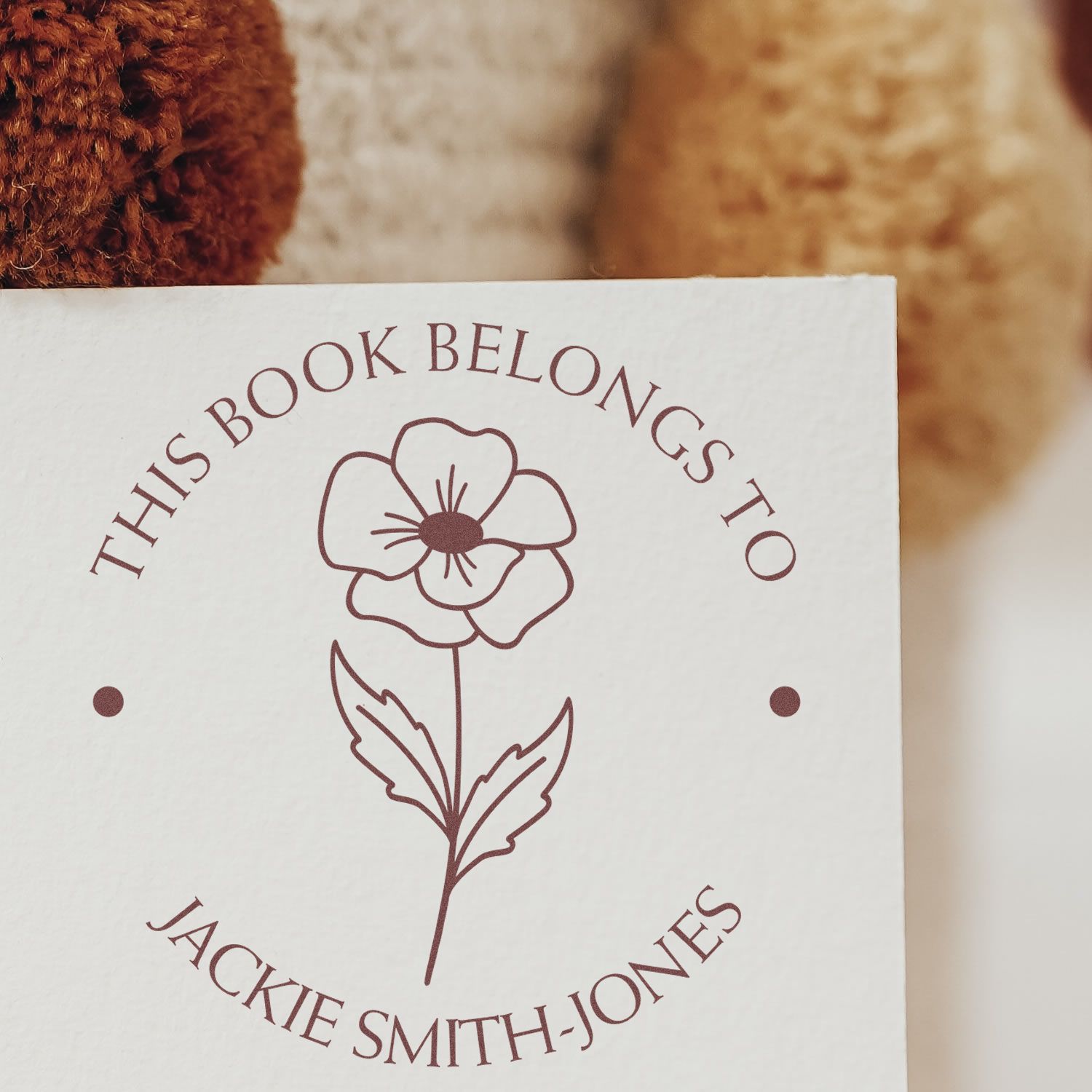 Maroon custom stamp seal with floral outline and This Book Belongs To Jackie Smith-Jones on white paper.