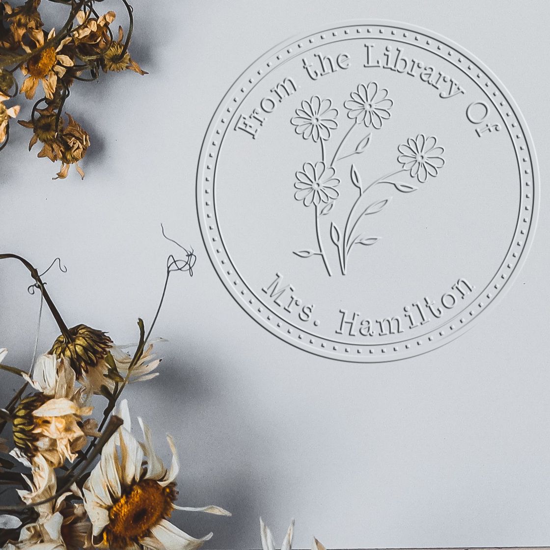 Shiny floral stamps featuring a colorful daisy bouquet design on a personal library paper embosser in use.