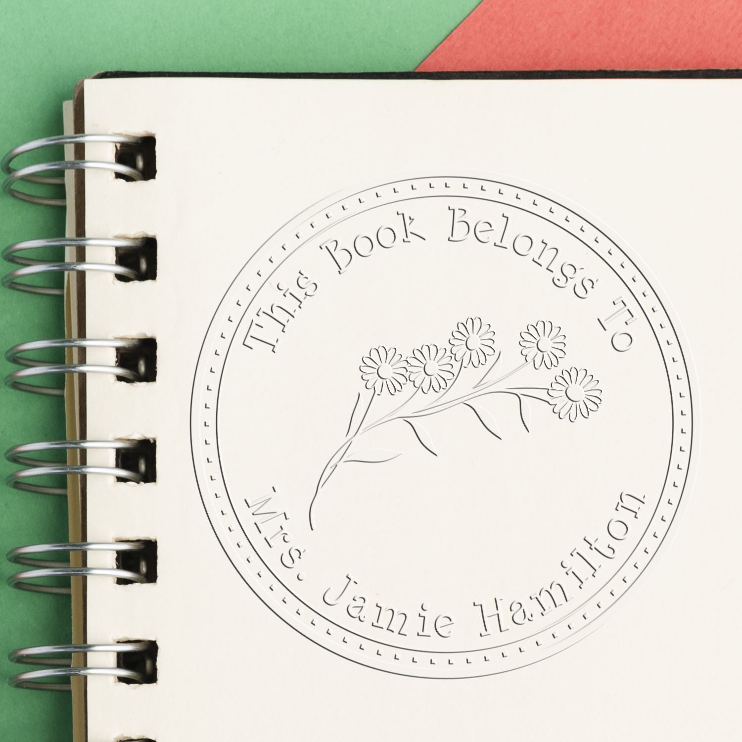 White spiral notebook with custom book-ownership embossing seal, floral circle design, and silver rings.