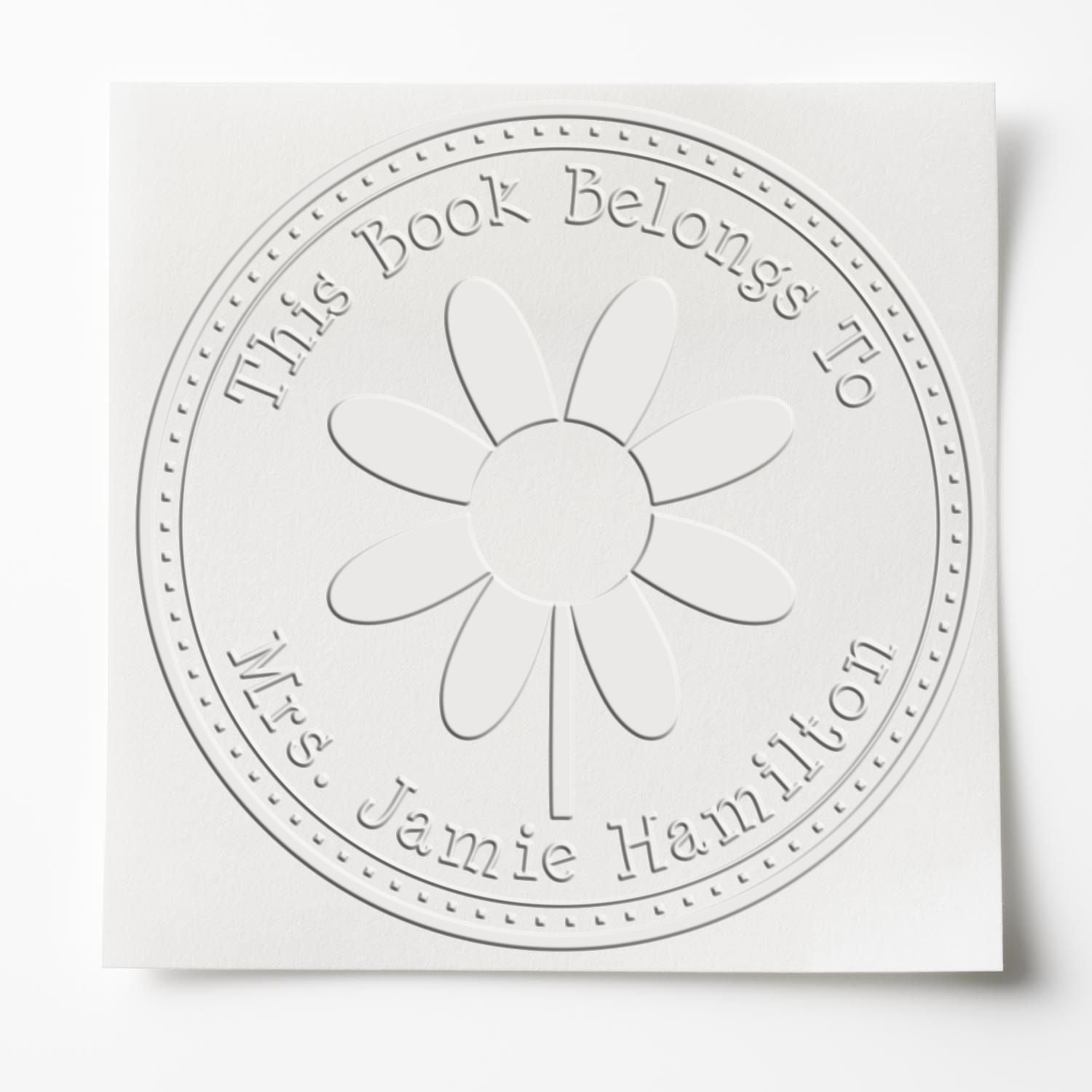 White embossed circular book stamp seal with daisy and gray text: This Book Belongs to Mrs. Jamie Hamilton.