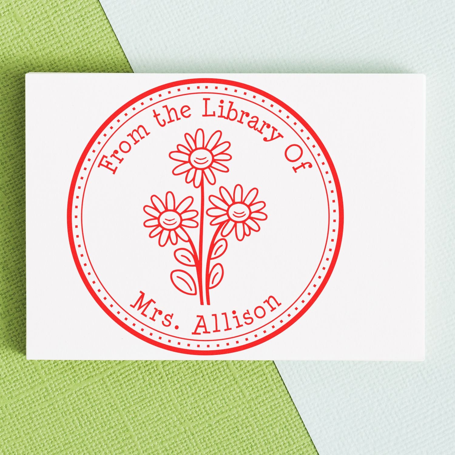 Red custom stamp seal with daisies, reading From the Library of Mrs. Allison, on a white card over green background.