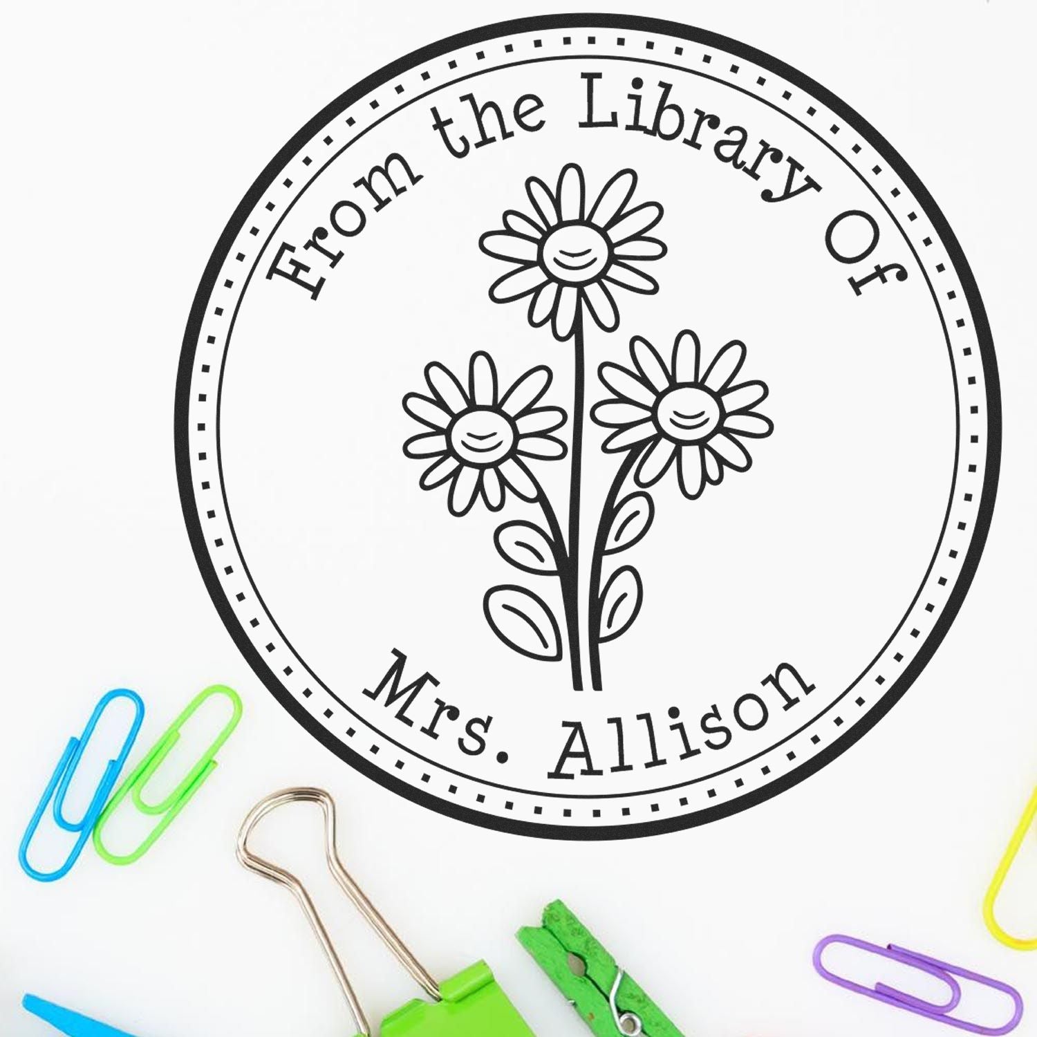 Black circular library stamp seal with daisies and From the Library Of Mrs. Allison, surrounded by colorful paper clips.