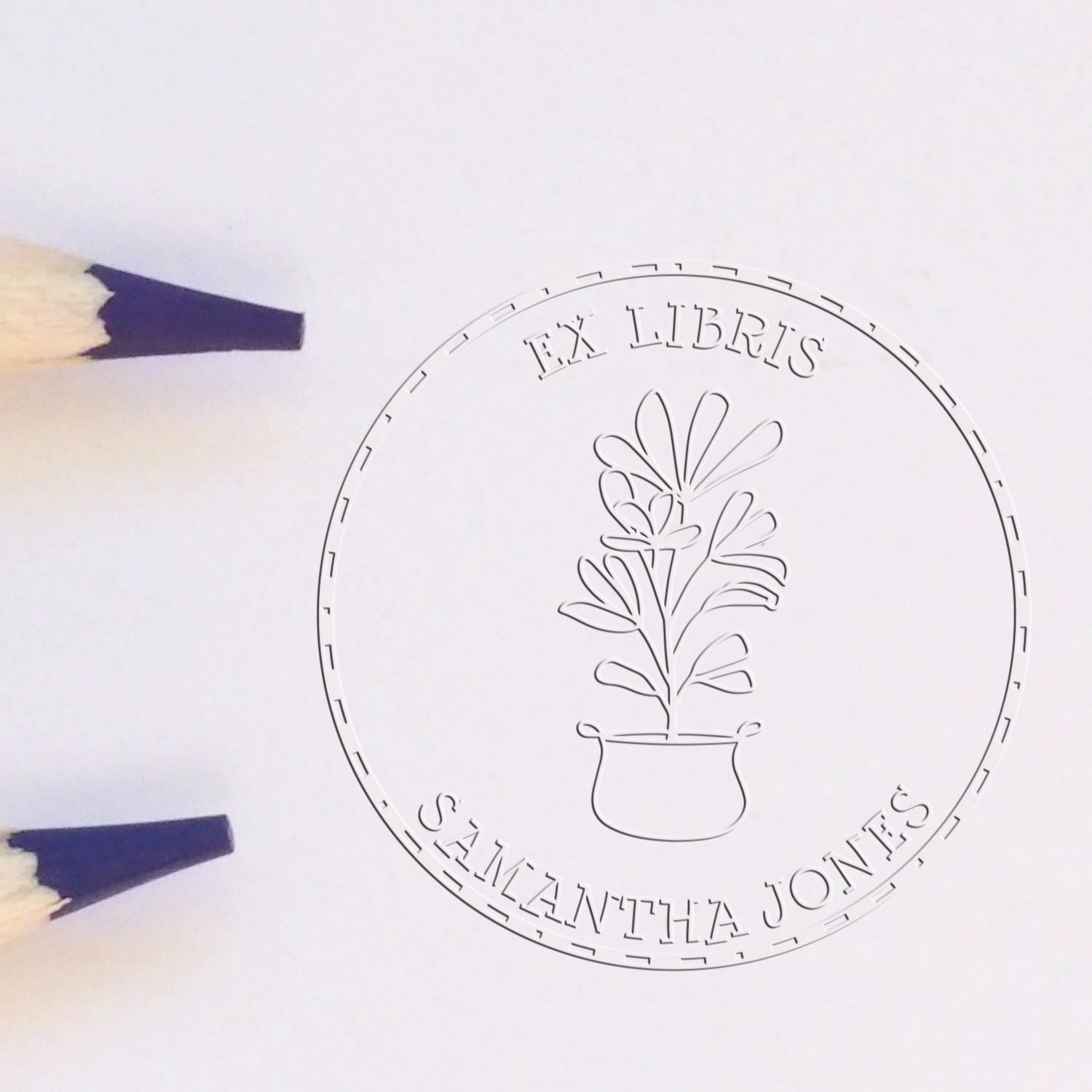 White circular embossing seal with plant-in-pot logo, text FX LIBRIS and Samantha Jones, beside two purple pencil tips.
