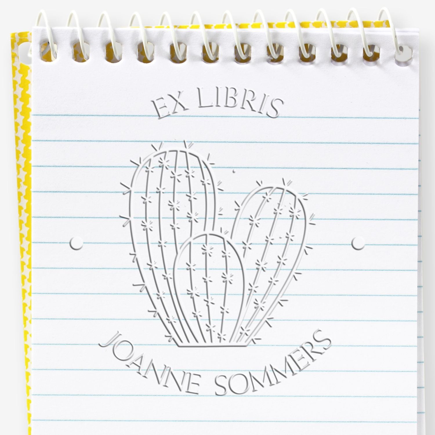 Embossed cactus ex libris stamp seal on a white spiral notebook with blue lines and a yellow patterned border.