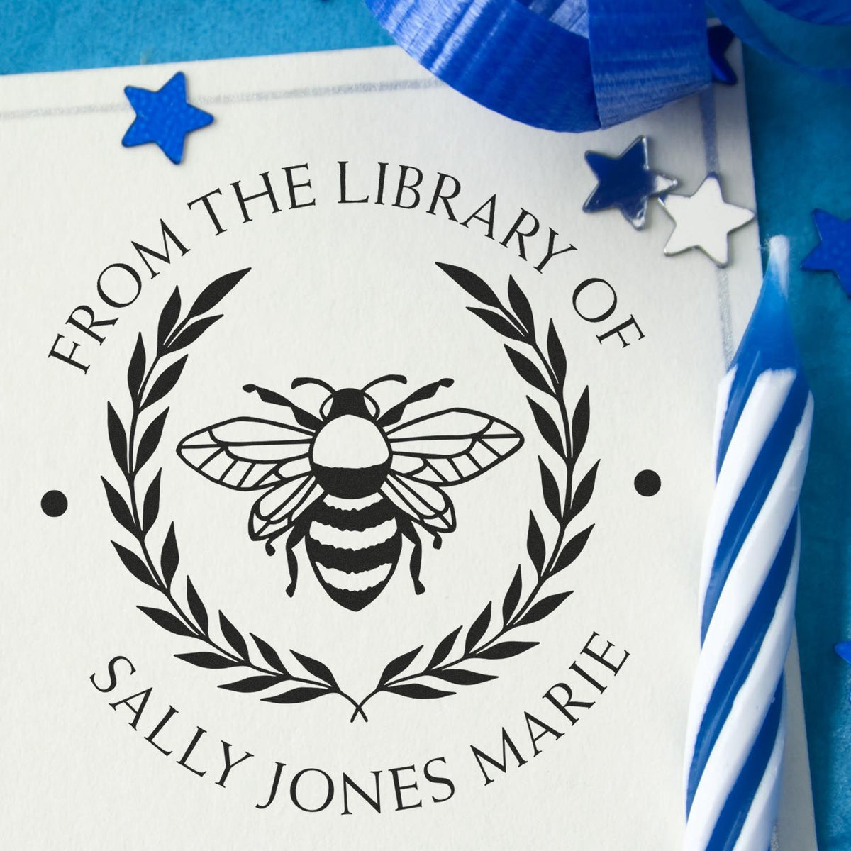 Custom library stamp seal with black bee and laurel on white paper, accented by blue stars and ribbon.