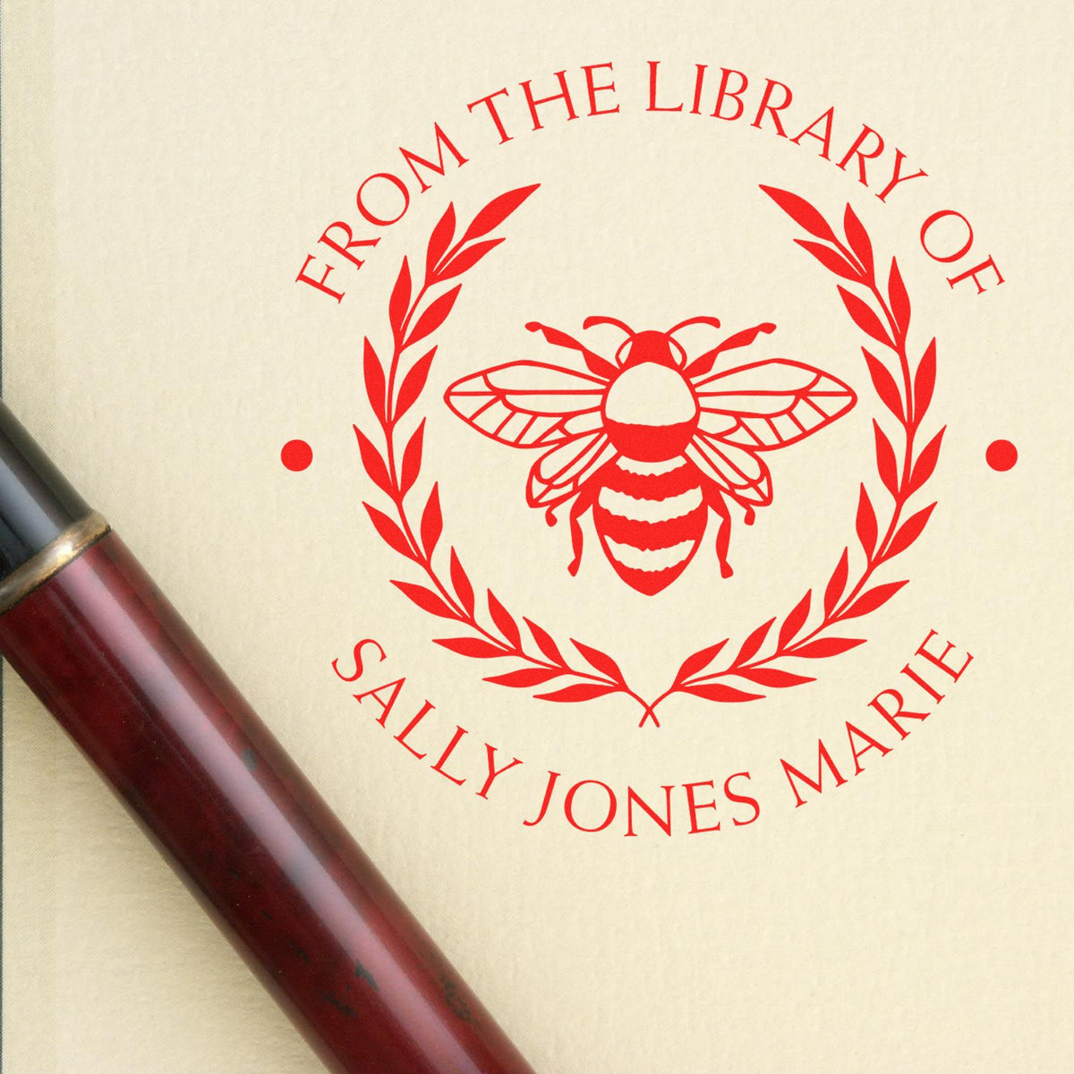 Red From the Library of Sally Jones Marie stamp seal with bee and laurel wreath on cream, maroon handle.