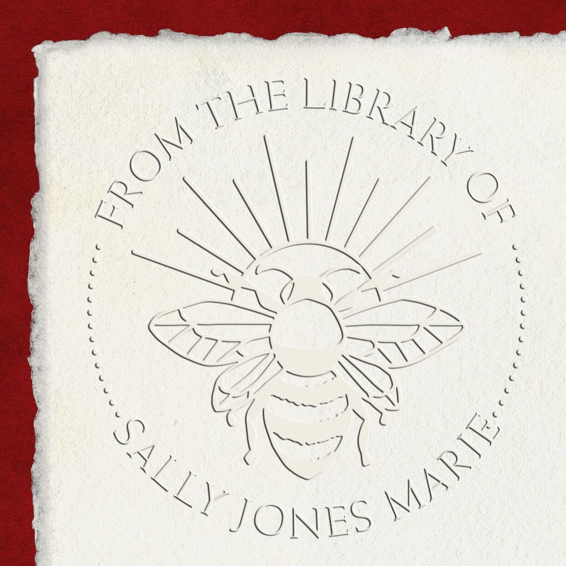 White embossed library seal stamp with bee design and From the Library of Sally Jones Marie on red background.