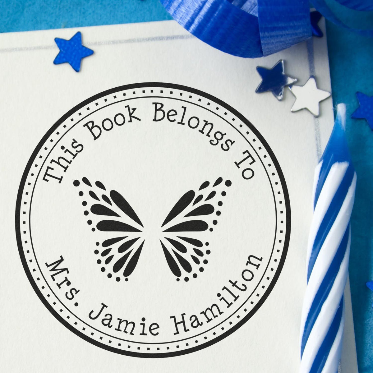 Black circular book ownership stamp and seal with butterfly, personalized name, on white paper with blue stars and ribbon.