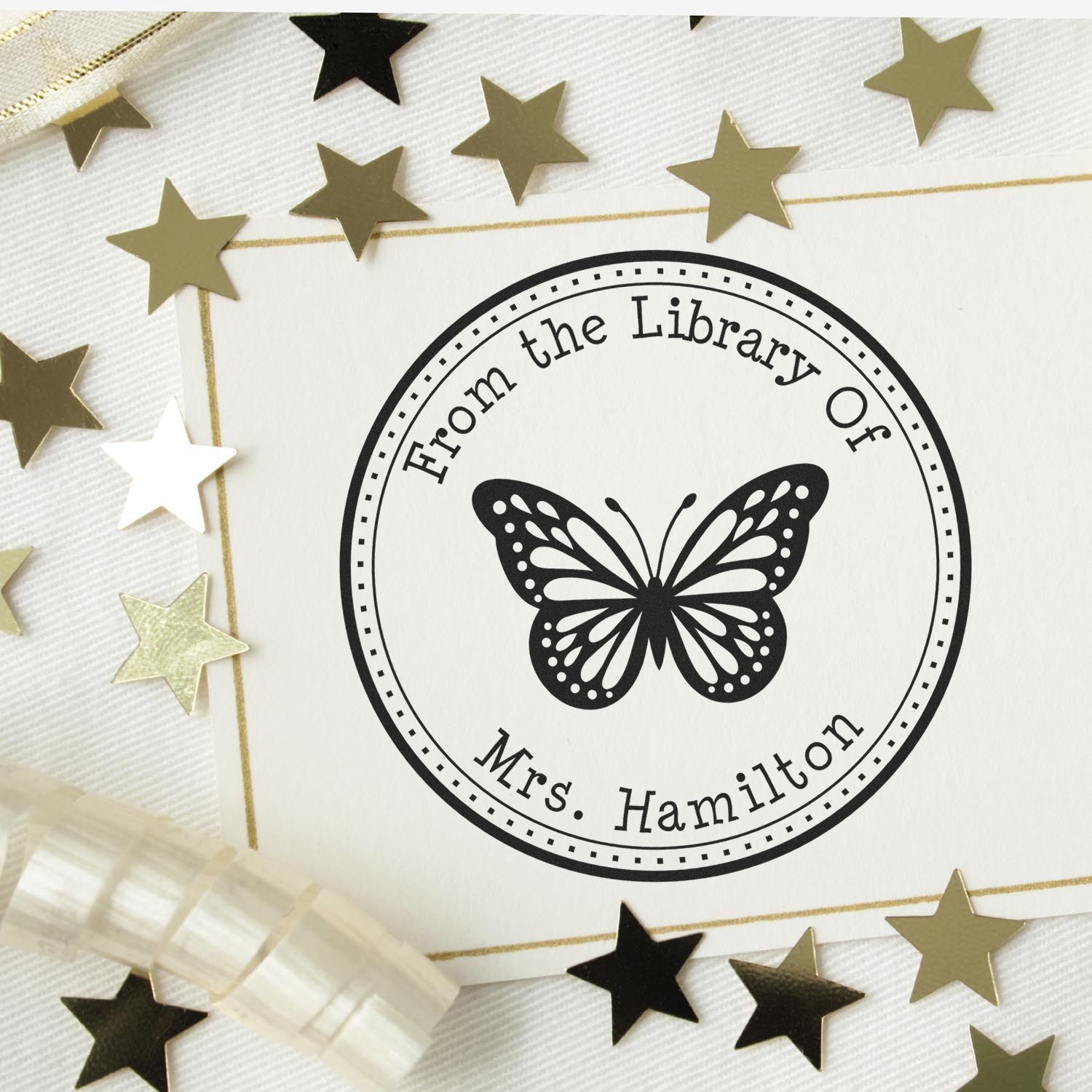 Custom round library stamp seal with black butterfly, Mrs. Hamilton text, and gold star accents on a white background