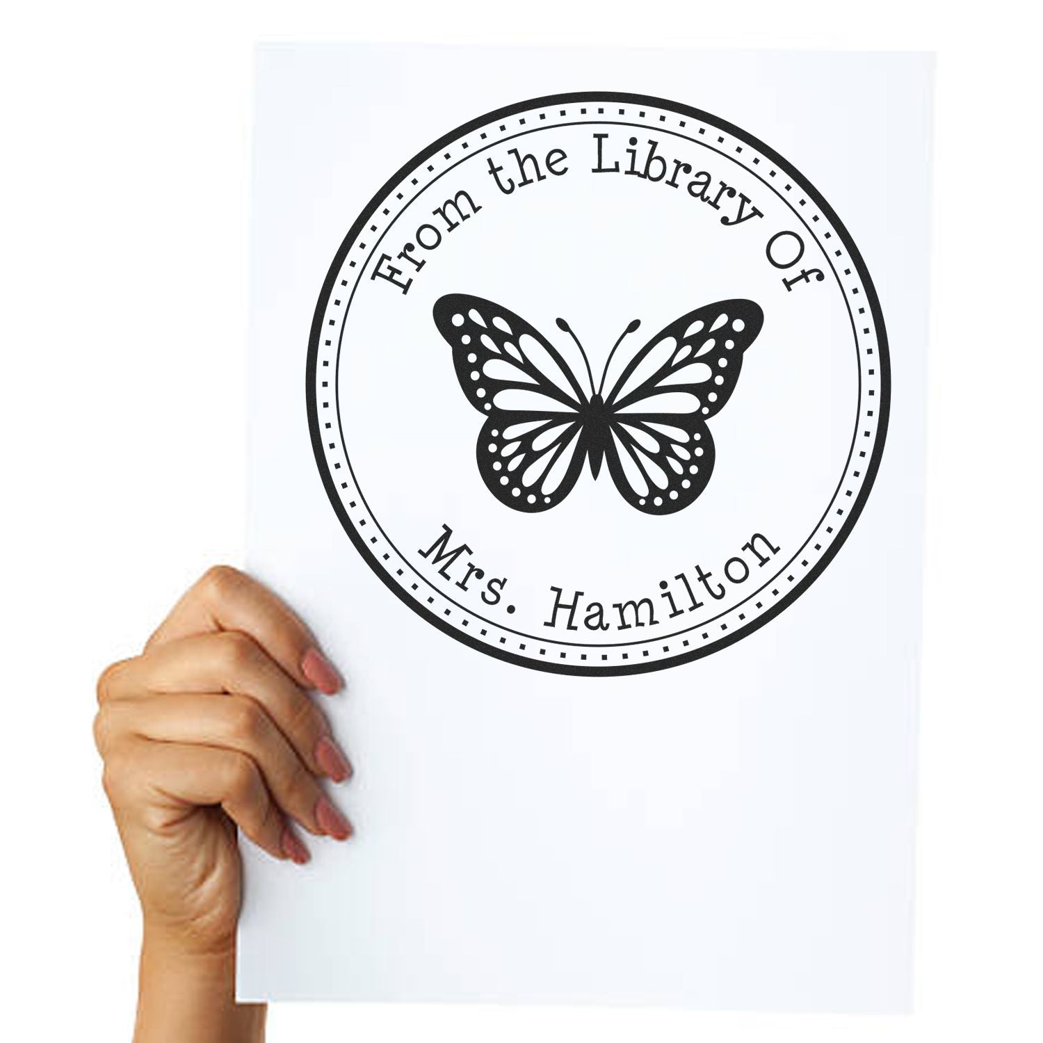 Black circular library stamp and seal with butterfly, reading From the Library Of Mrs. Hamilton, on white paper.