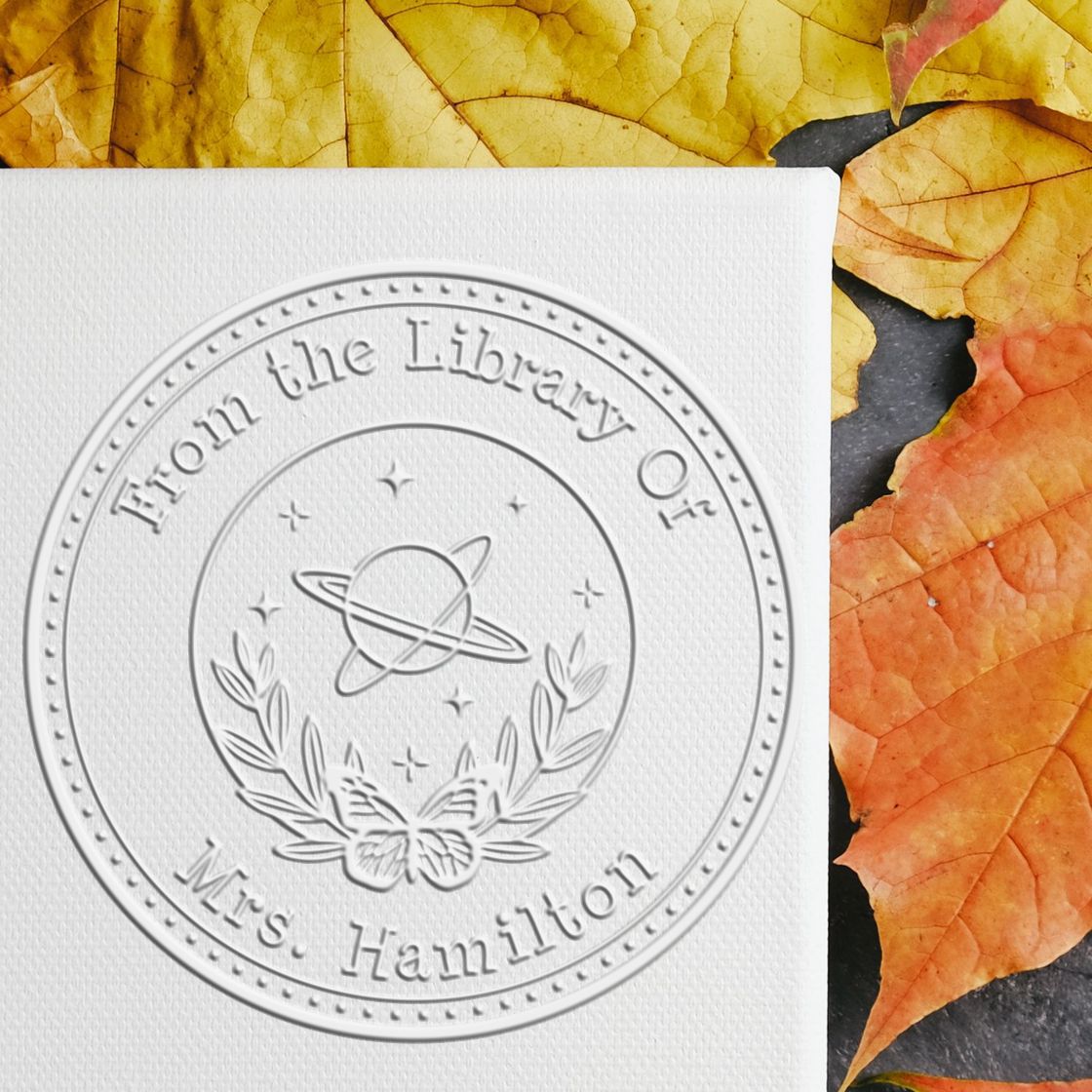 Custom white embossed round library stamp seal on textured paper, framed by yellow and orange autumn leaves.