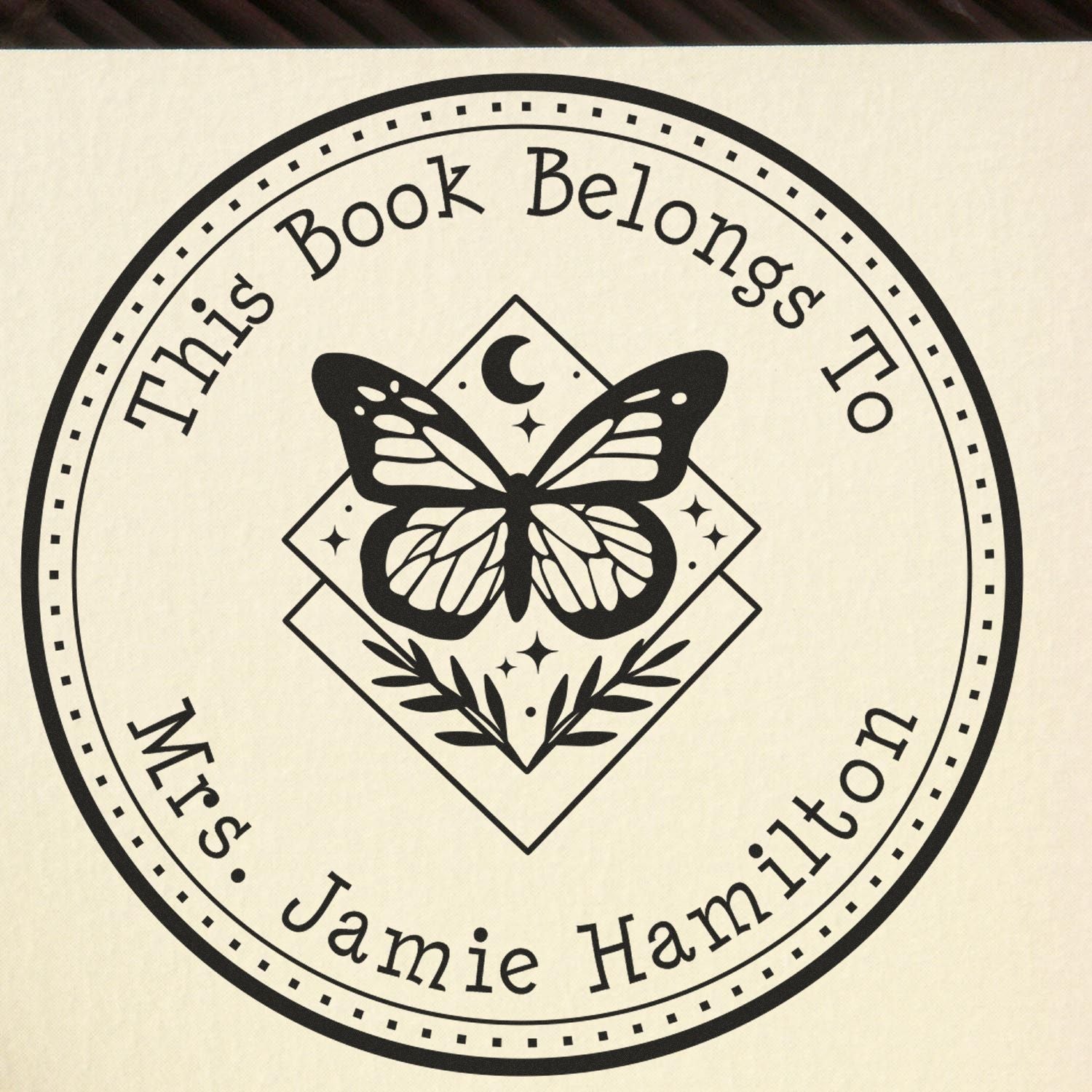 Black custom book stamp and seal with butterfly, moon, and floral design on cream background for Mrs. Jamie Hamilton.