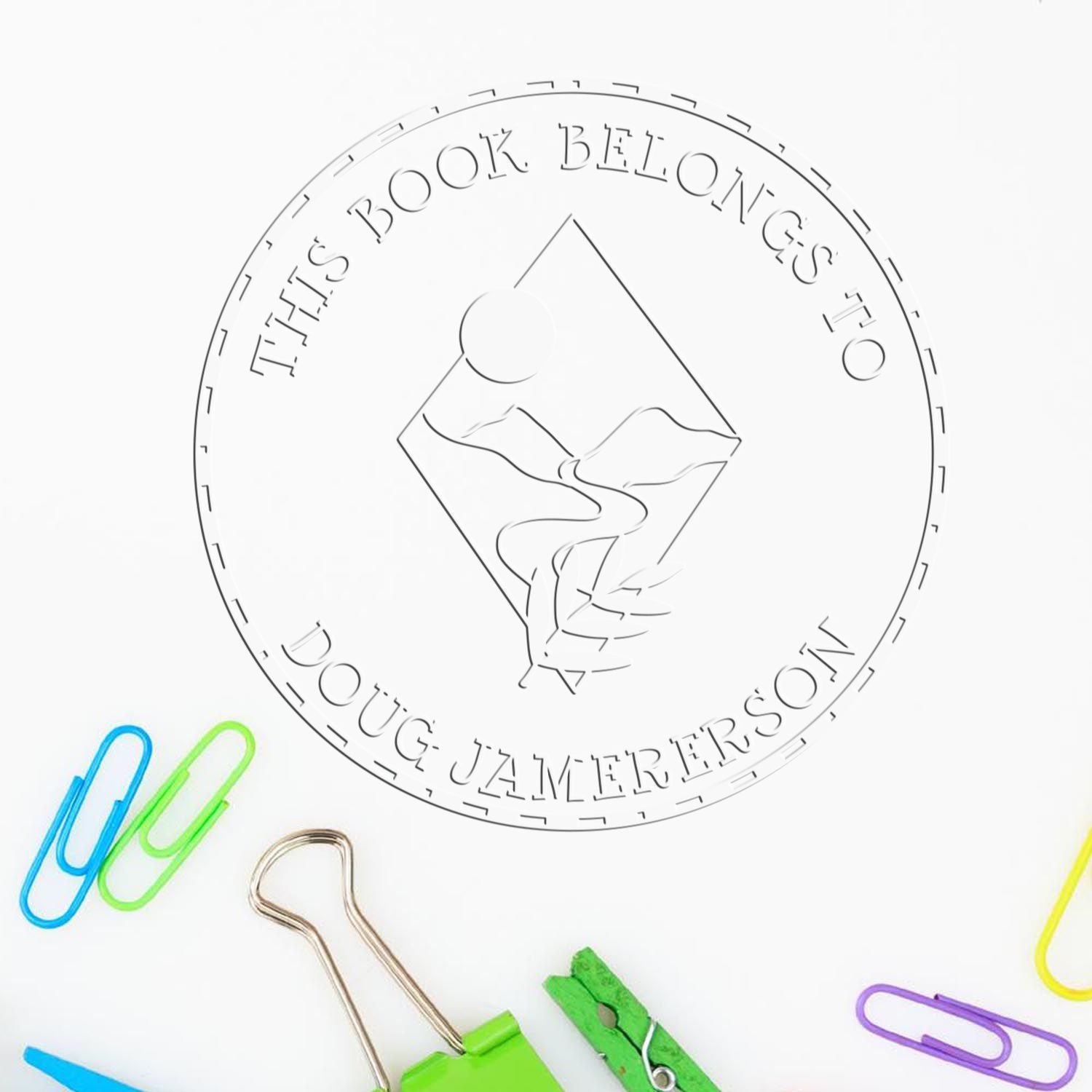 White circular book stamp and seal with engraved text and mountain logo, surrounded by colorful paper clips.