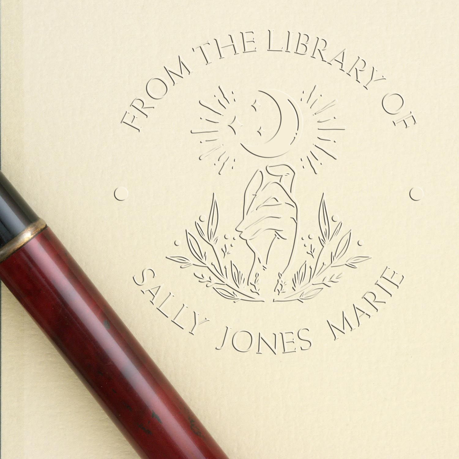 Cream library embossing stamp seal with rose and moon motif, reading From the Library of Sally Jones Marie, burgundy handle.
