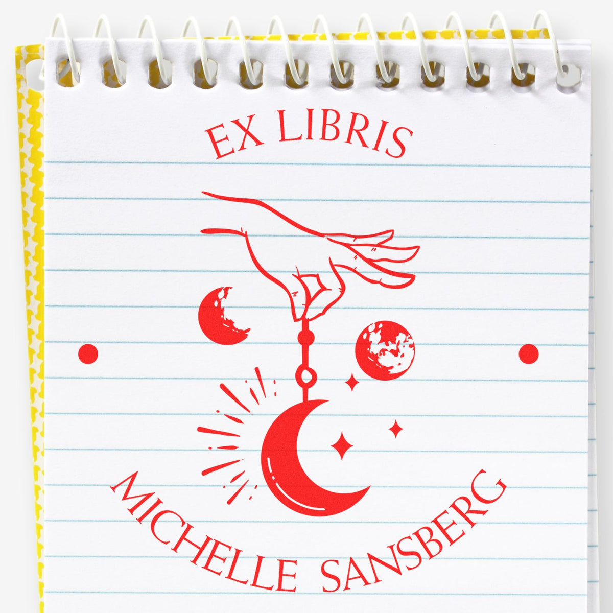 Red Ex Libris bookplate stamp and seal on a spiral notebook page, with a hand, crescent moon, and stars in bright red.