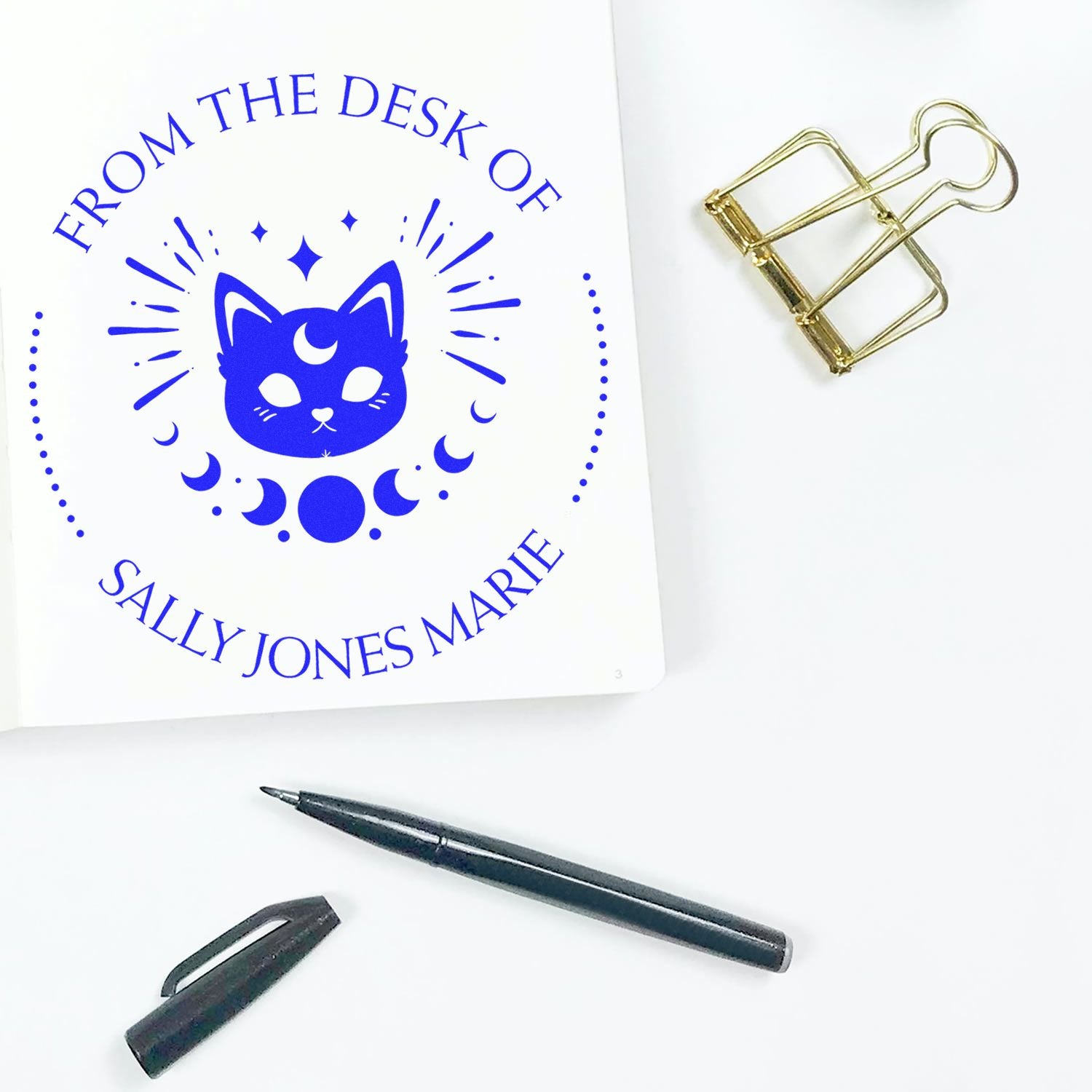 Blue cat-and-moon custom stamp design on white card, with gold binder clip and black pen for seal products.