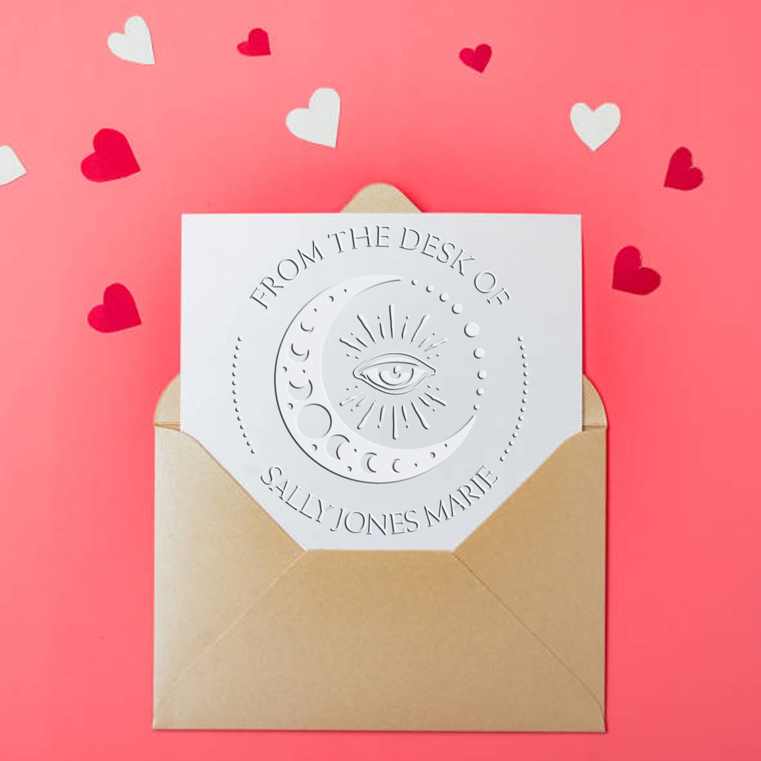 White embossed custom seal stamp on a tan envelope, with eye and moon design, against a pink background with heart confetti.