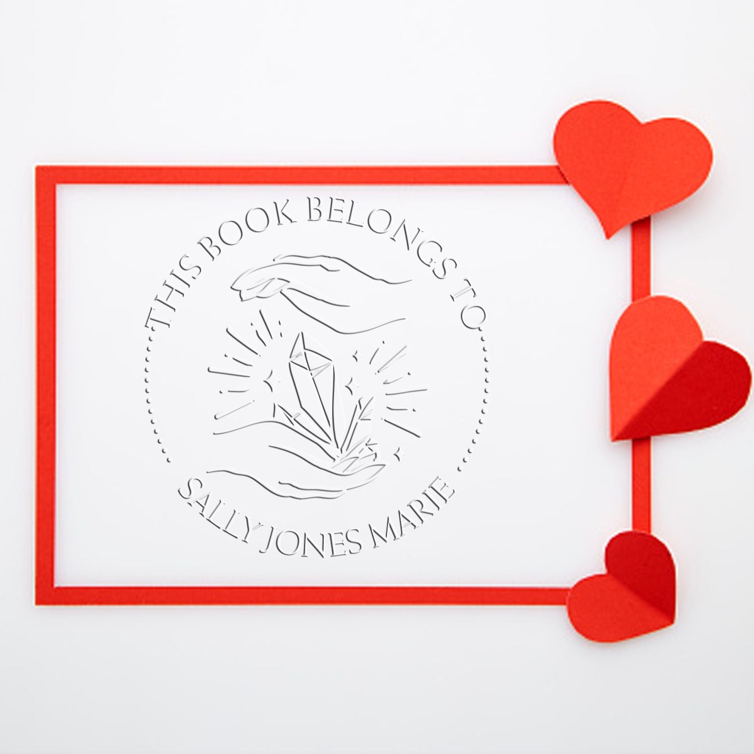 Red custom stamp and seal with heart corners, reading This Book Belongs To Sally Jones Marie and crystal design.
