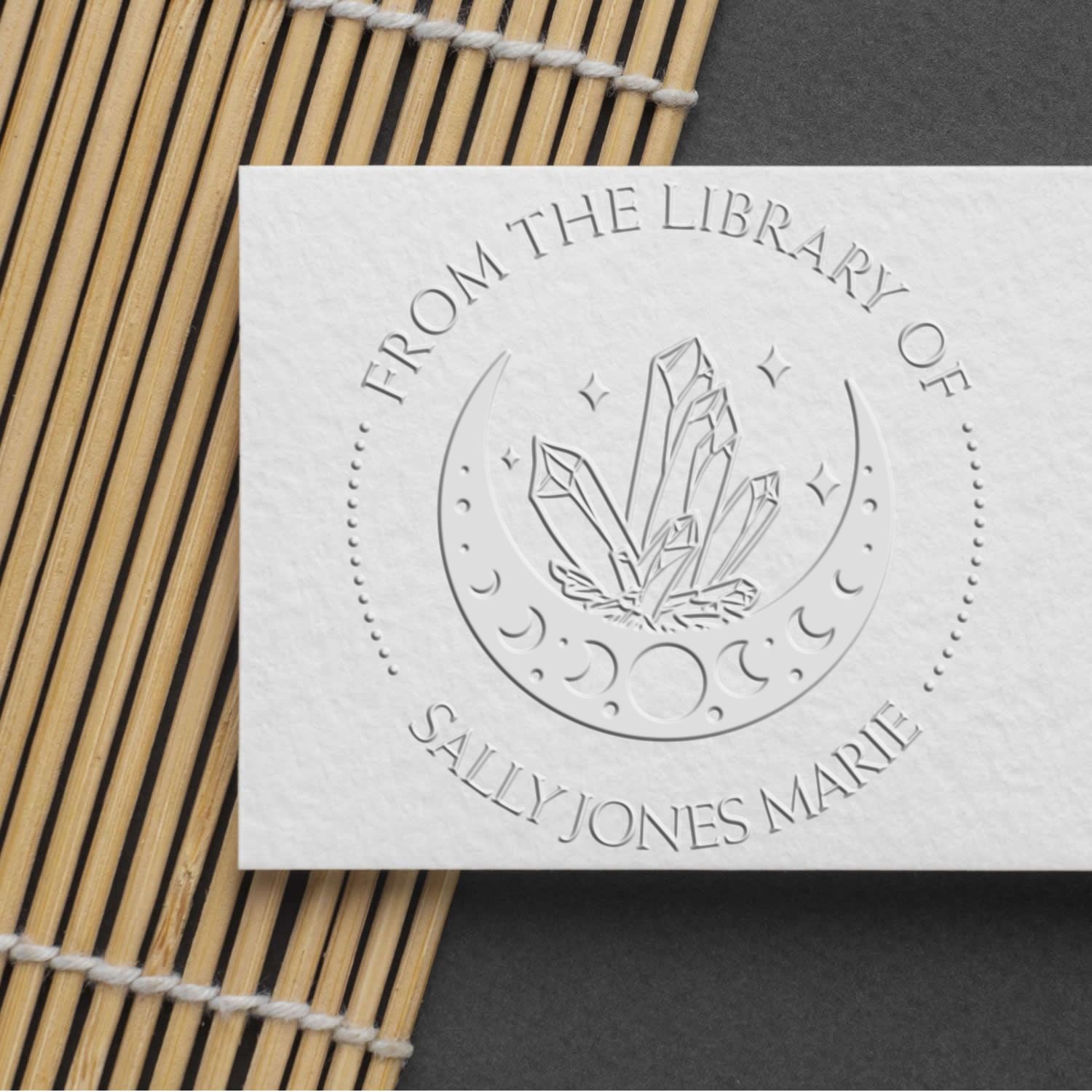Embossed white stamp seal with crescent moon and crystals, labeled Sally Jones Marie, on a dark background.
