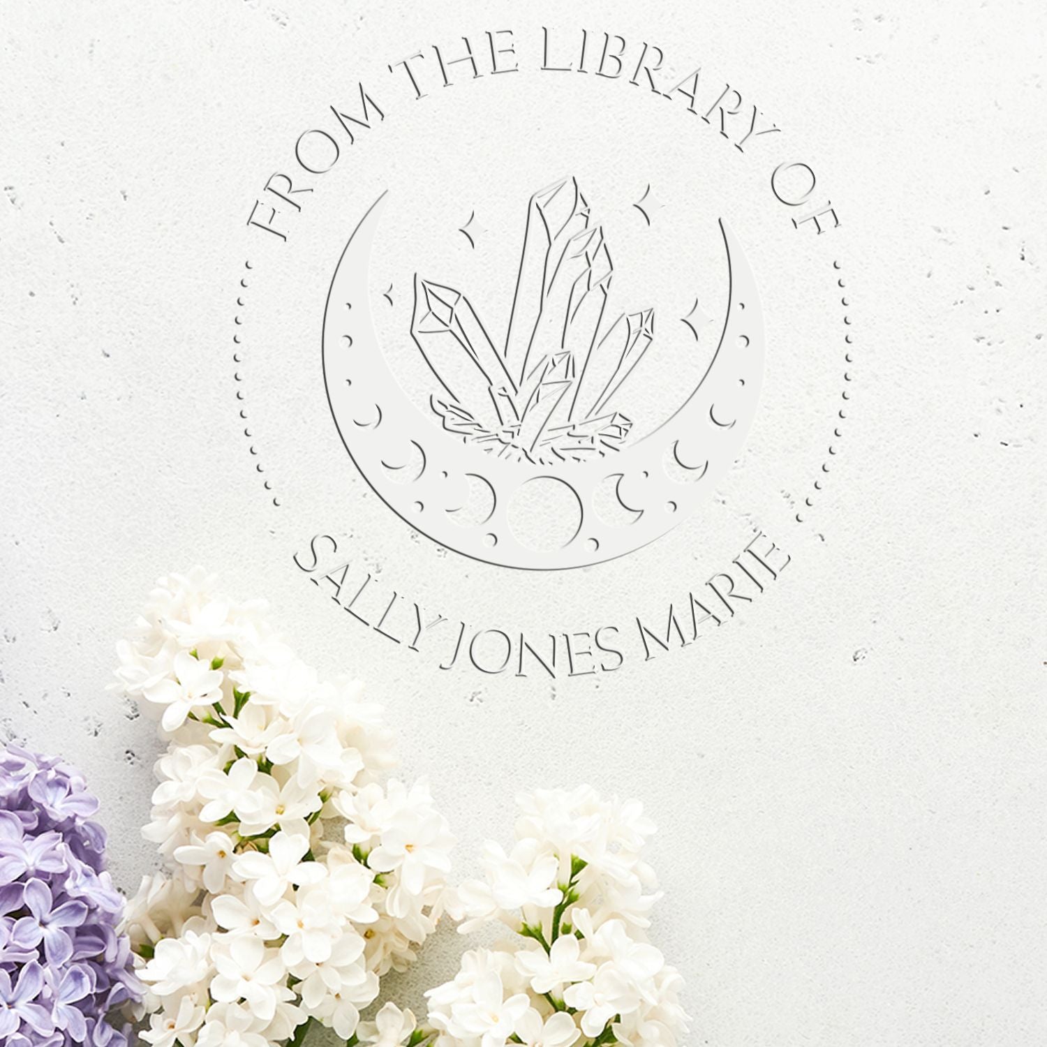 Embossed white library stamp seal with crystal logo, curved text, and white and lilac flowers on textured paper.