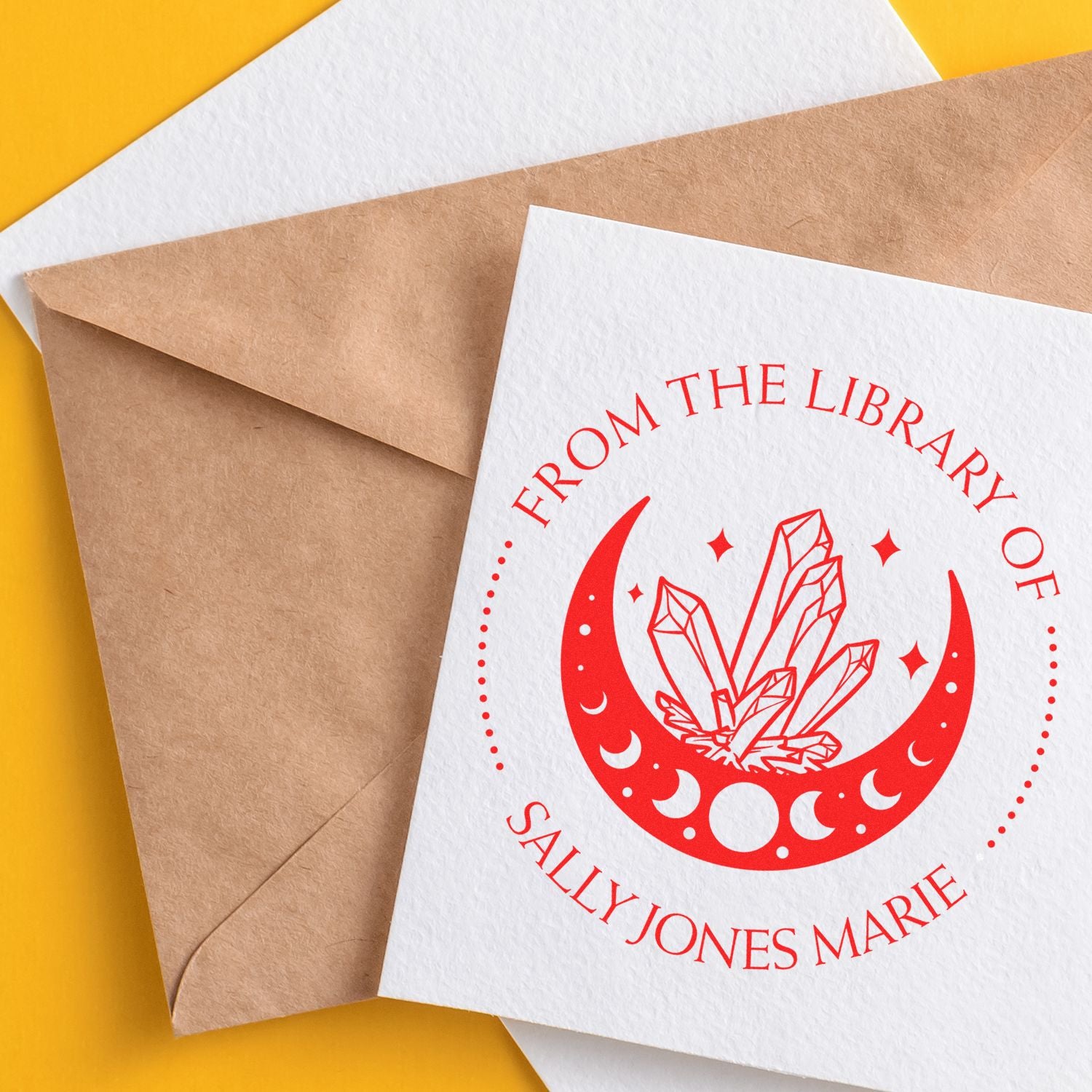 Red custom library stamp and seal on white card, with moon and crystal design over a kraft envelope on yellow background.