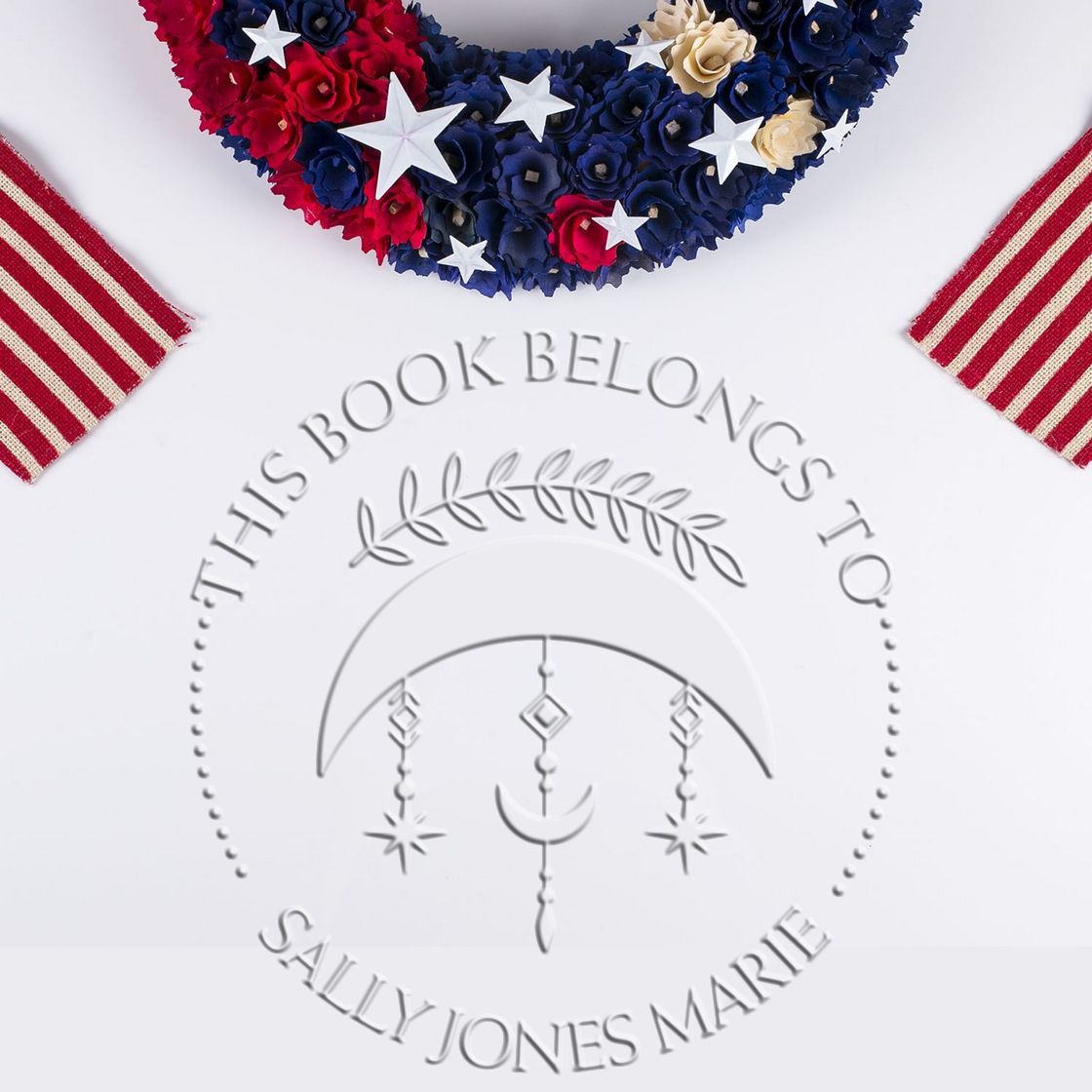 Embossed silver bookplate stamp seal with patriotic red, navy, and cream floral stars, reading This Book Belongs to Sally Jones Marie.