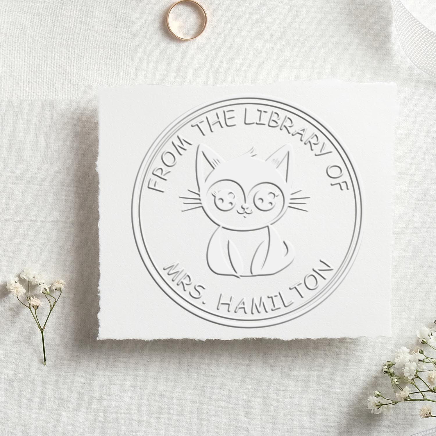 Custom round library stamp seal with a cute cat, embossed in white on cream fabric, reading From the Library of Mrs. Hamilton.