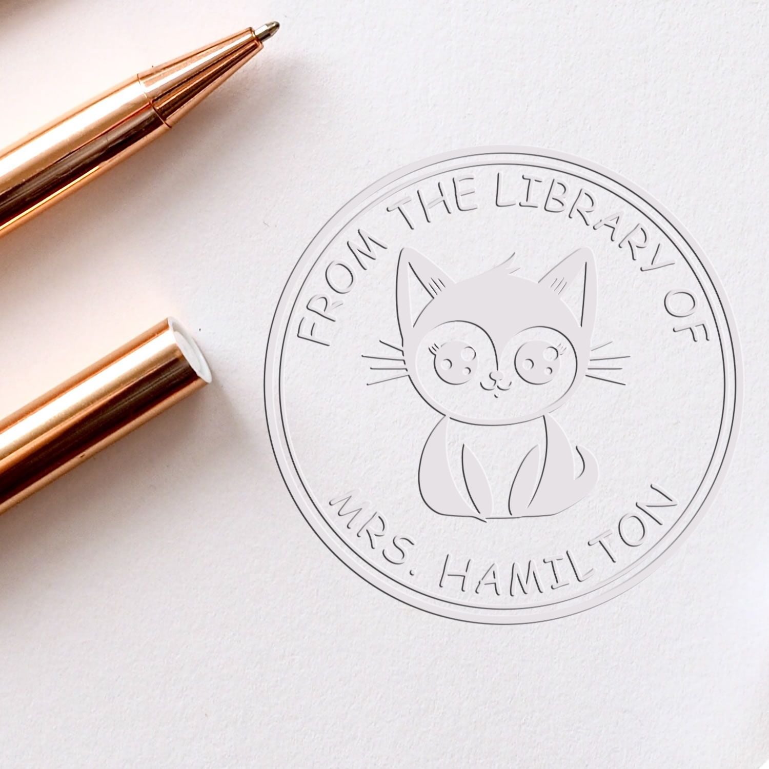 Rose gold stamp and seal tool beside a white cat library embossing seal for Mrs. Hamilton.