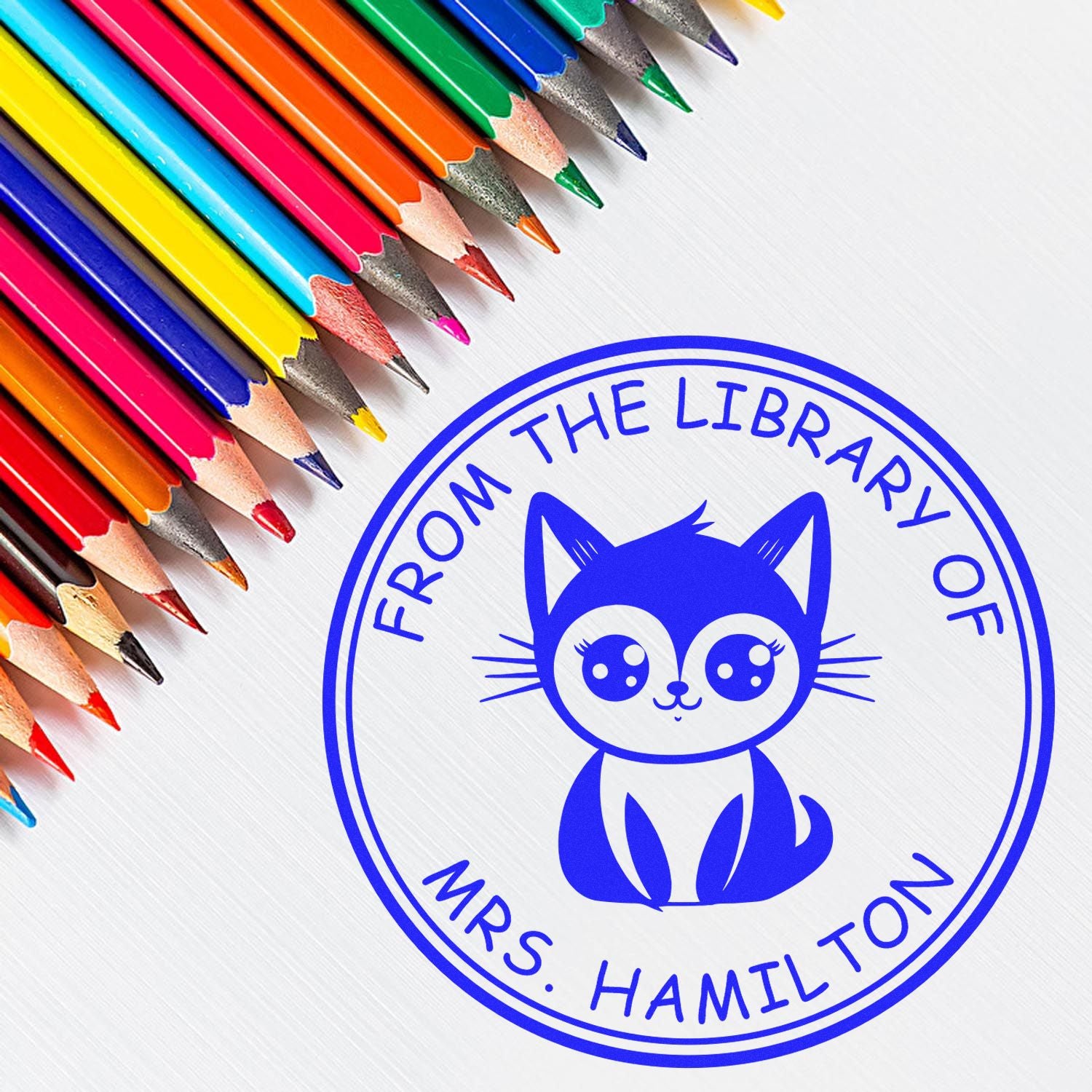 Colorful pencils next to a blue cat library stamp seal reading From the Library of Mrs. Hamilton.