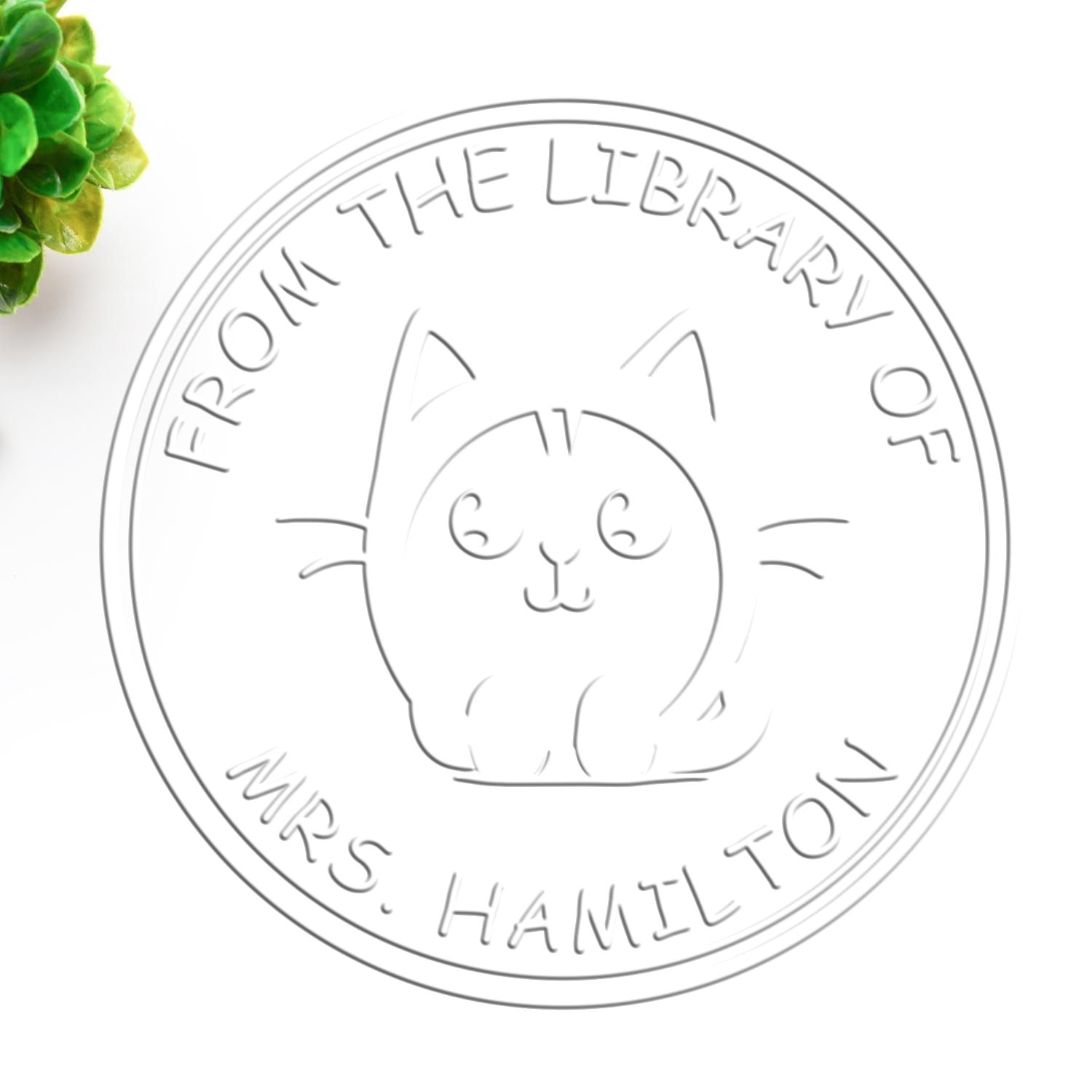 Gray embossed circular stamp seal with cat face and From the Library of Mrs. Hamilton text, plus green leaves.