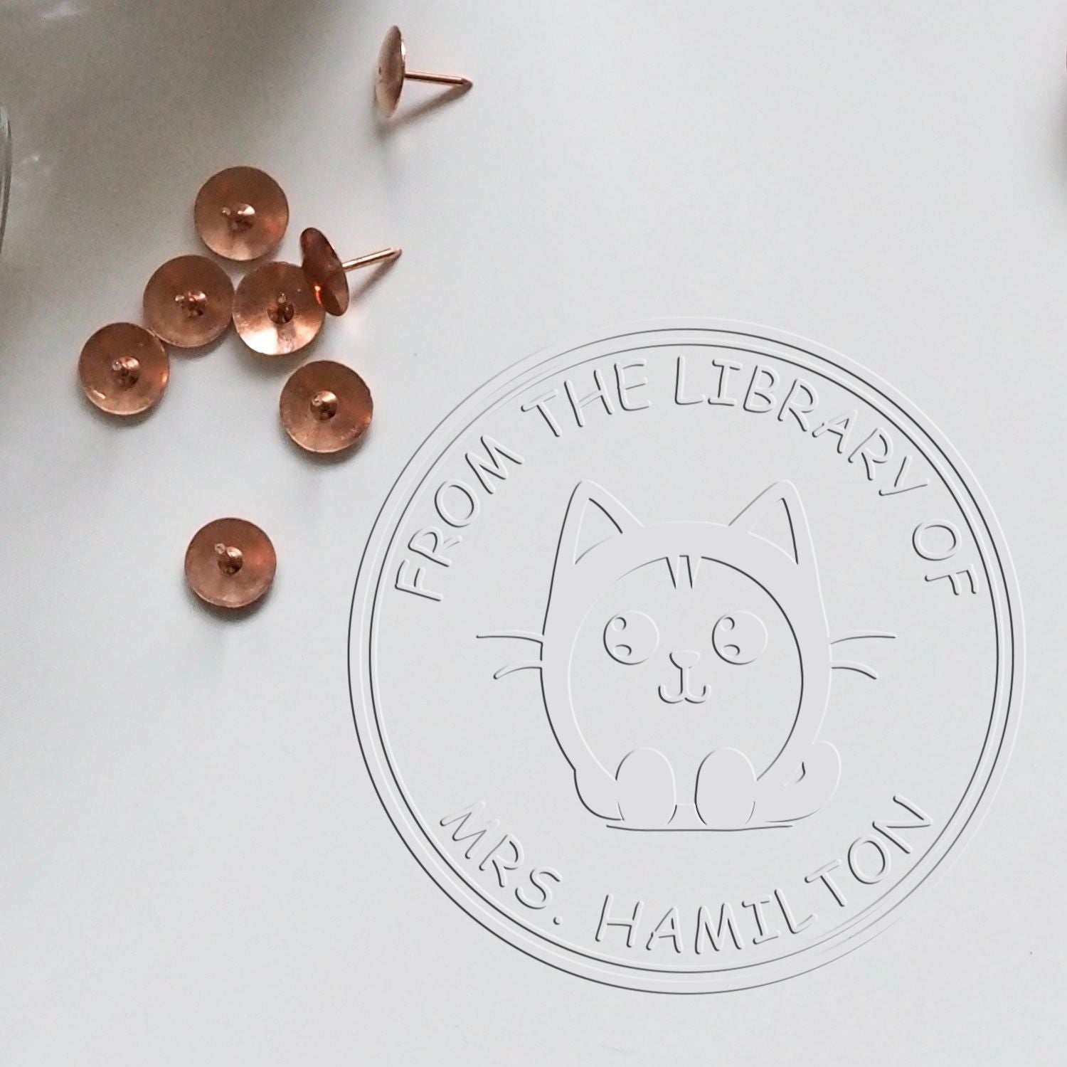 Copper sealing wax stamps beside a white embossed cat library seal reading "From the Library of Mrs. Hamilton".