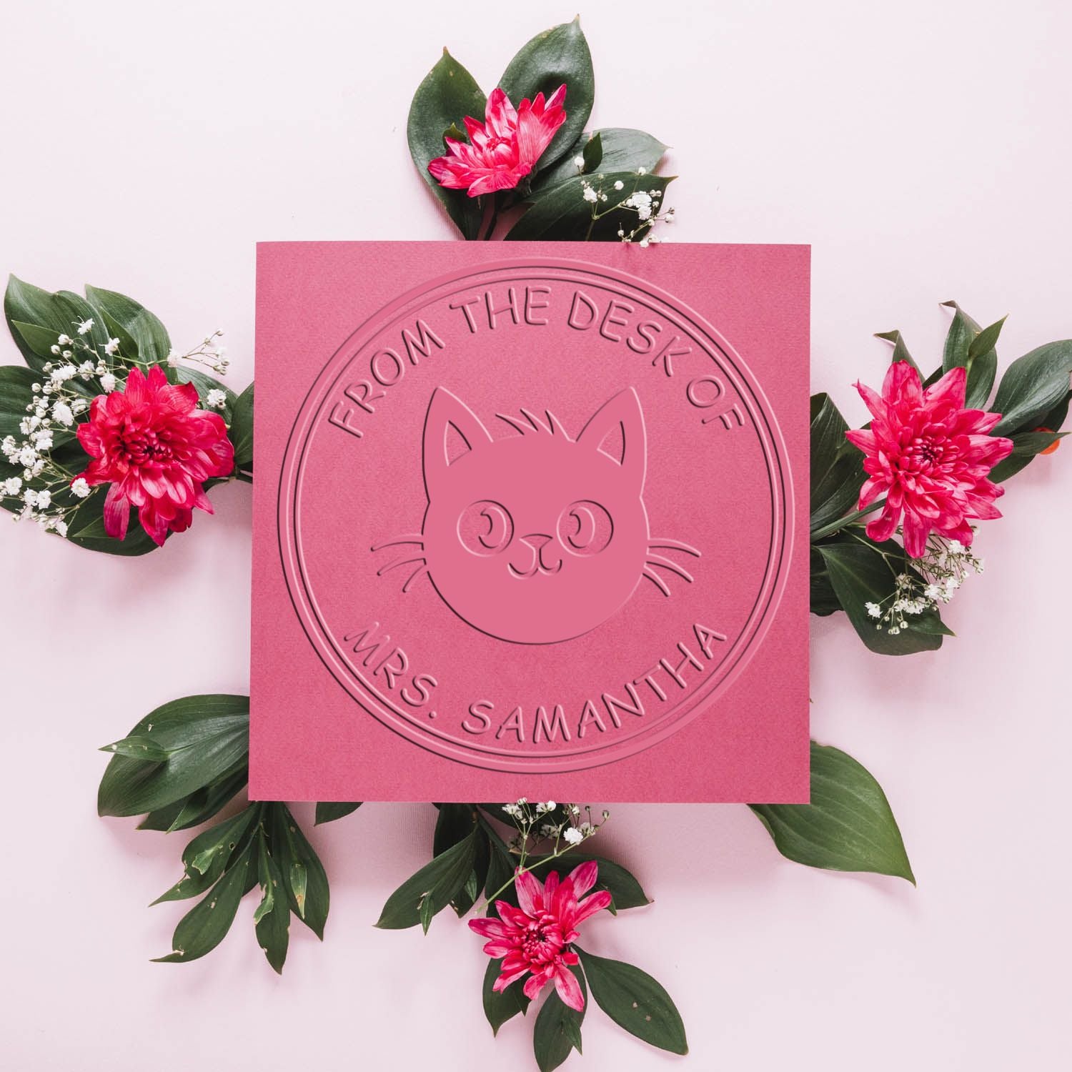 Pink embossed cat stamp seal reading From the Desk of Mrs. Samanthia, framed by green leaves and bright pink flowers.