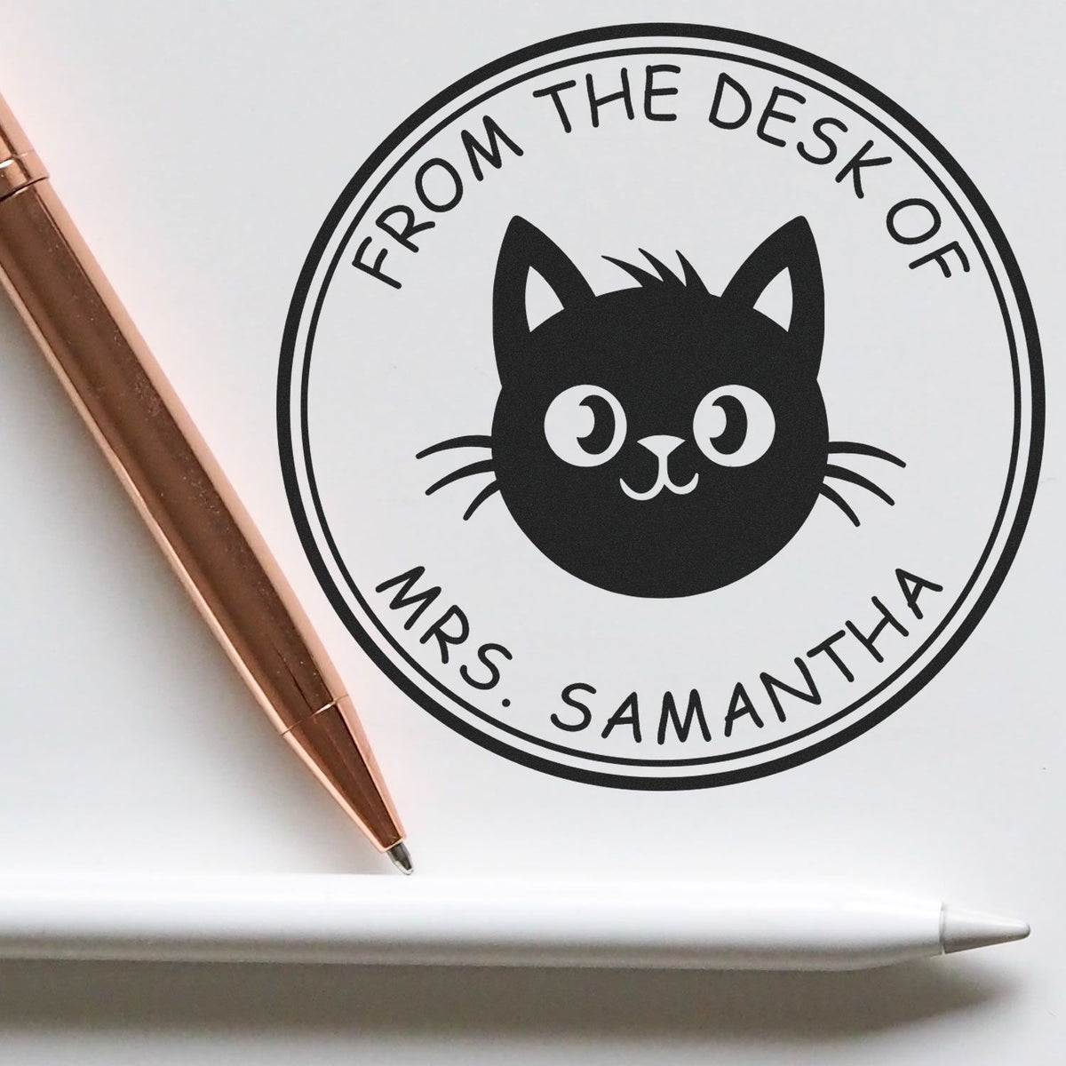 Black cat desk seal stamp reading From the Desk of Mrs. Samantha on white paper with rose gold pen and white stylus.