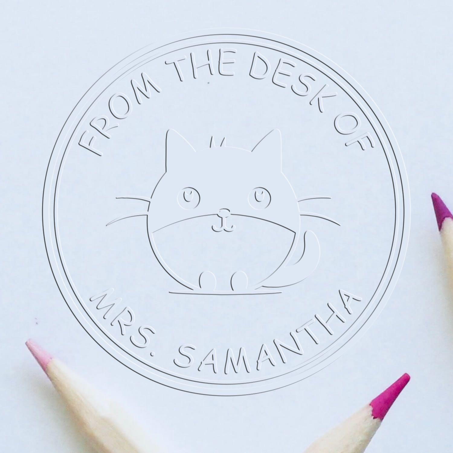 Embossed white circular cat seal stamp reading From the Desk of Mrs. Samantha, framed by pink-tipped pencils.