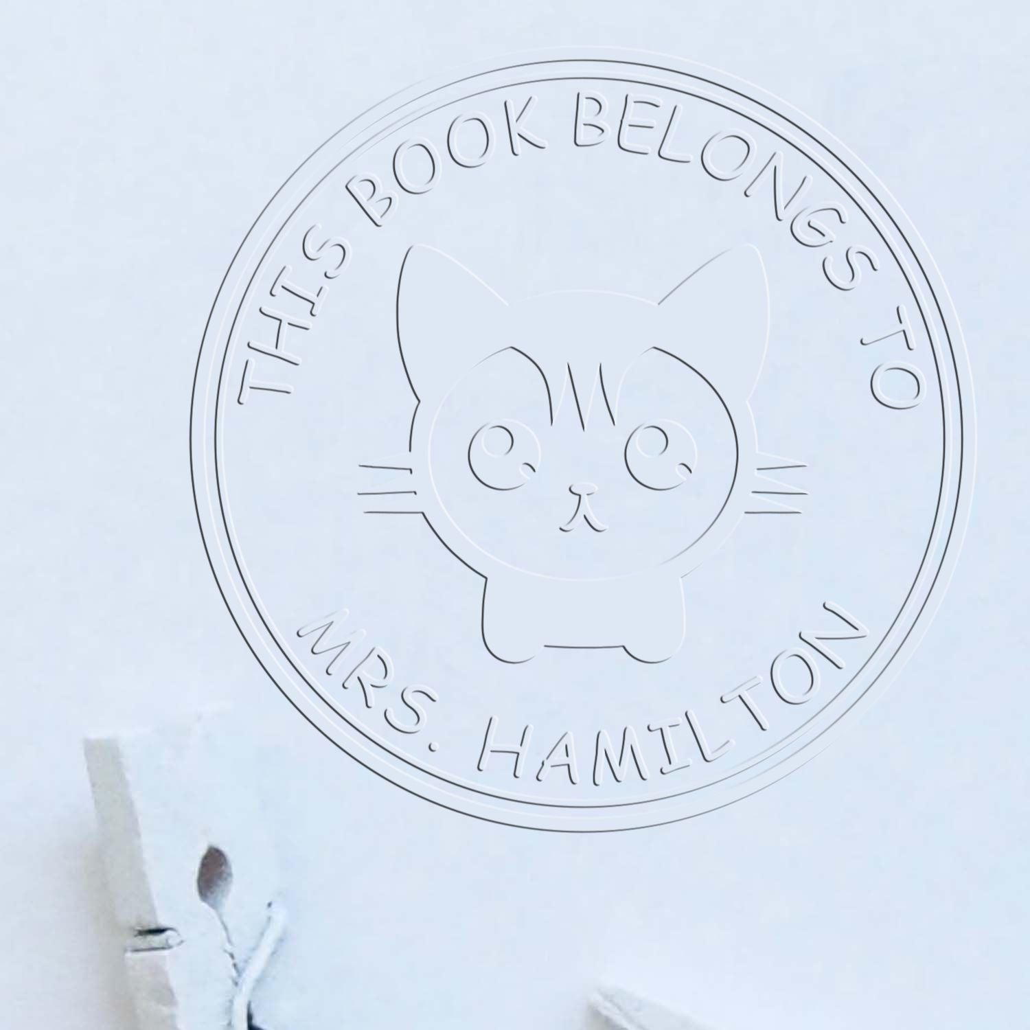Embossed pale blue book ownership stamp with cat seal, reading This Book Belongs to Mrs. Hamilton