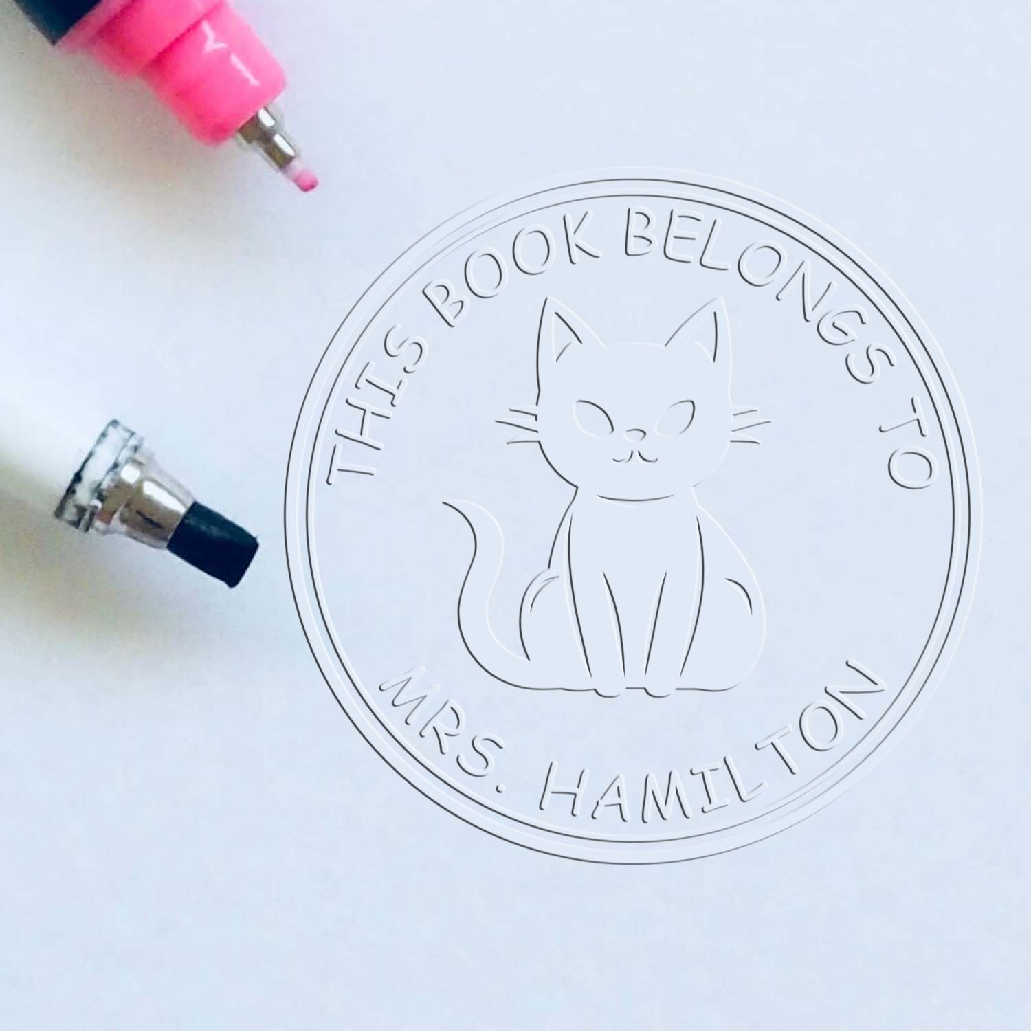 Pink and black stamp tips beside a clear circular cat book seal reading This Book Belongs to Mrs. Hamilton.