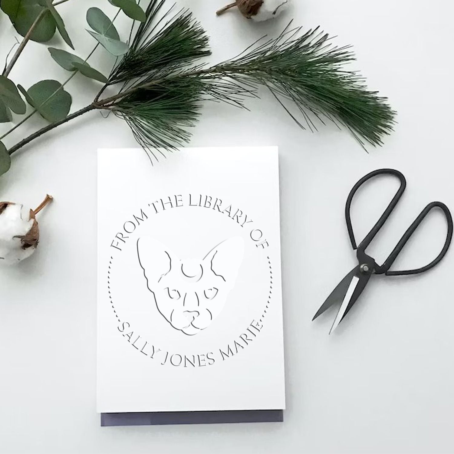 Custom white stamp and seal card with embossed dog portrait, black scissors, and greenery on a white background.